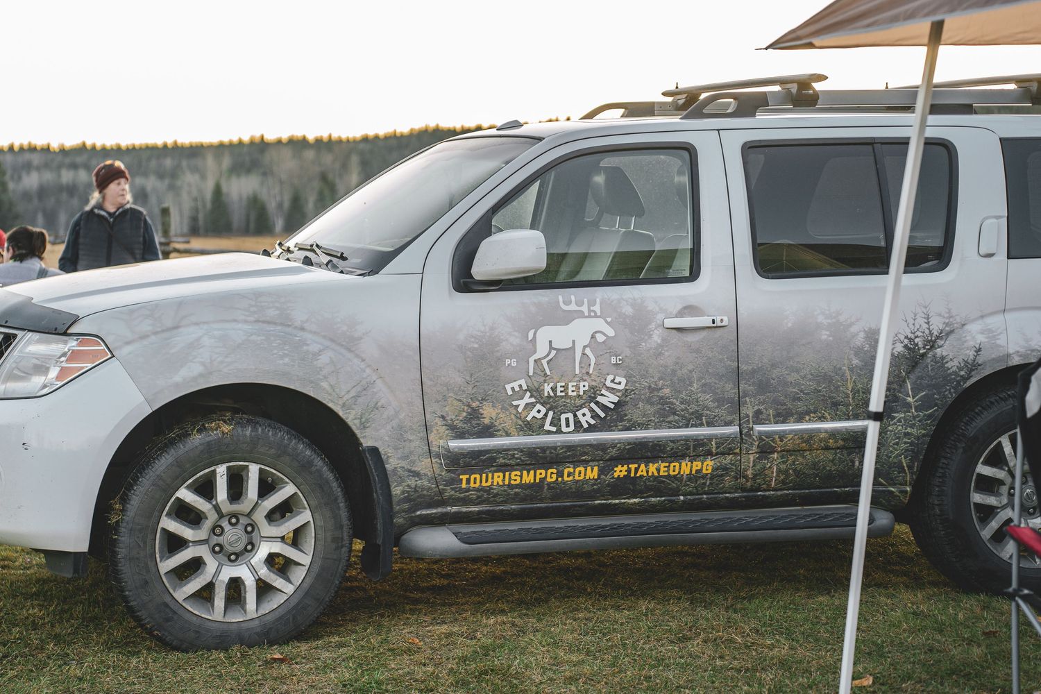Muddy Nissan Pathfinder with adventure exploration branding for Tourism Prince George, parked at an outdoor event at huble homestead.