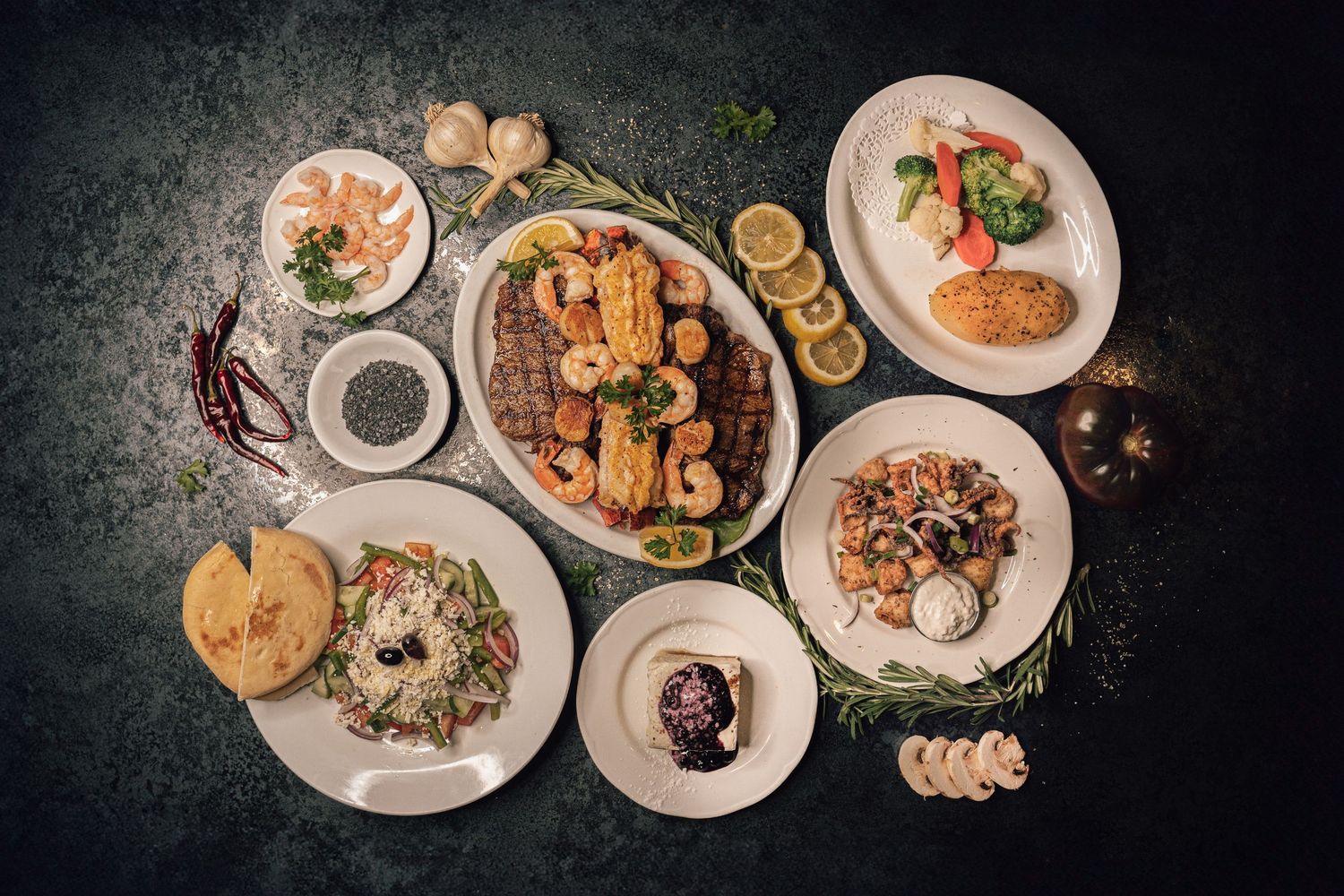 Overhead view of an elegant Mediterranean seafood spread with grilled shrimp, salads, and sides on white plates.
