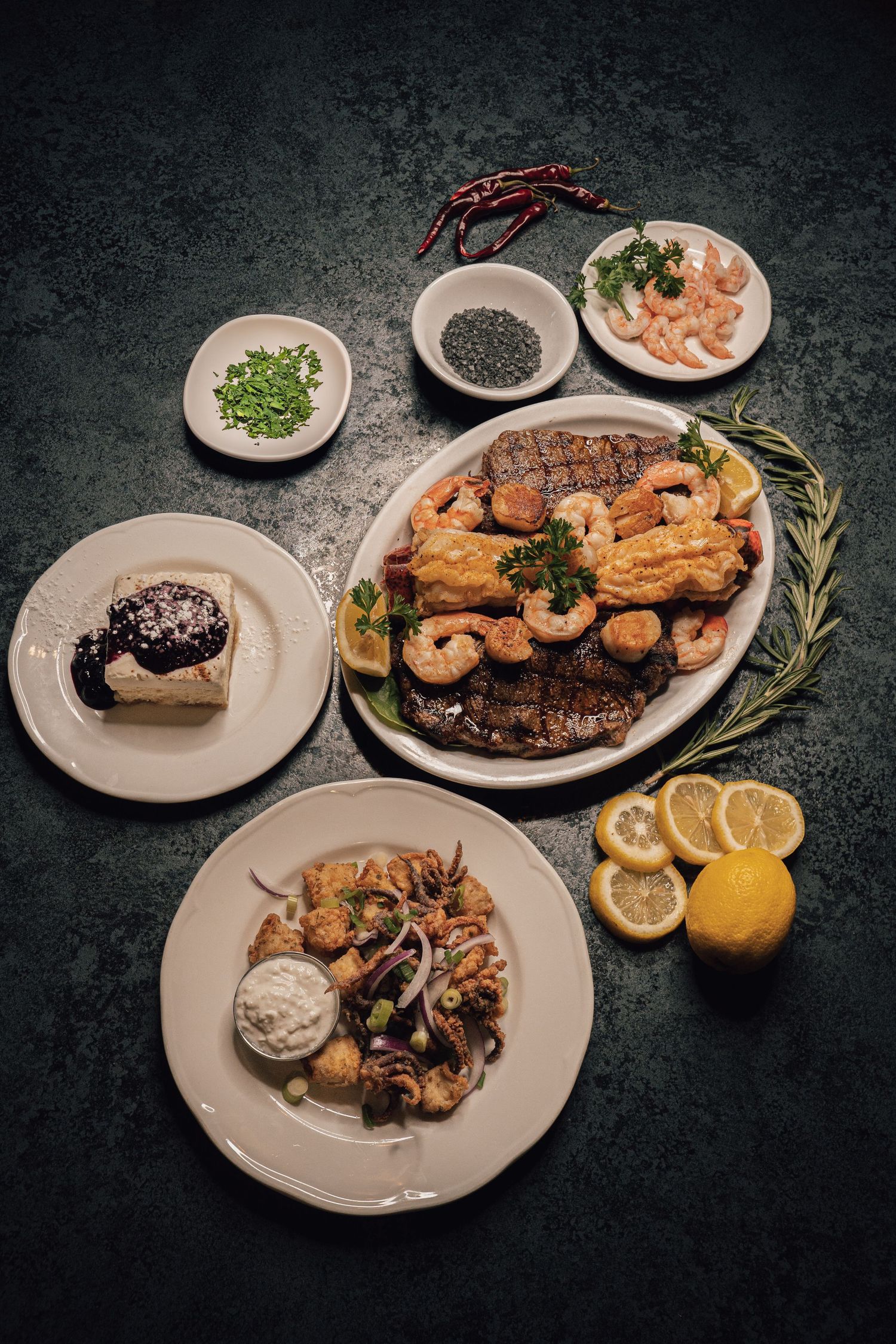 Elegant seafood spread with shrimp, grilled fish, calamari, and garnishes on a dark background.