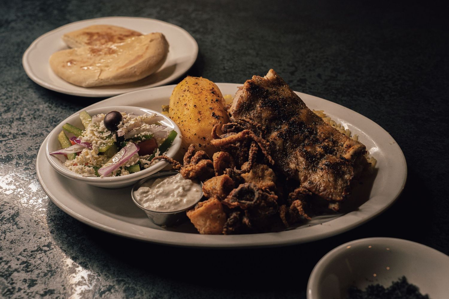 Mediterranean platter with crispy calamari, tzatziki, pita bread, and garnishes on a marble surface.