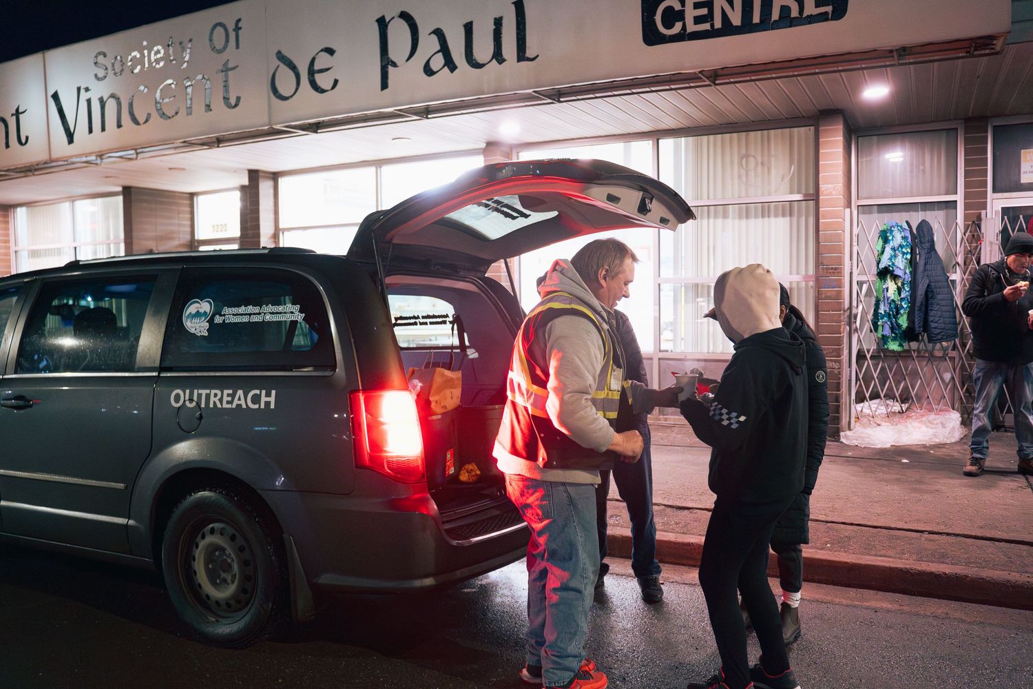 Outreach workers unload supplies from a van outside a Society of St. Vincent de Paul center at night.