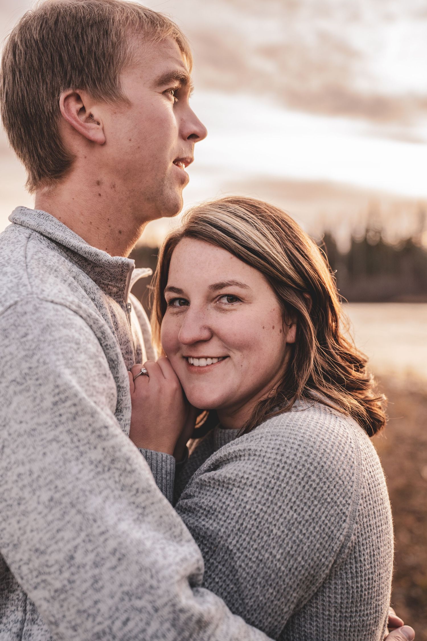 Smiling woman rests her head on her partners chest during a warm golden hour engagement photo.