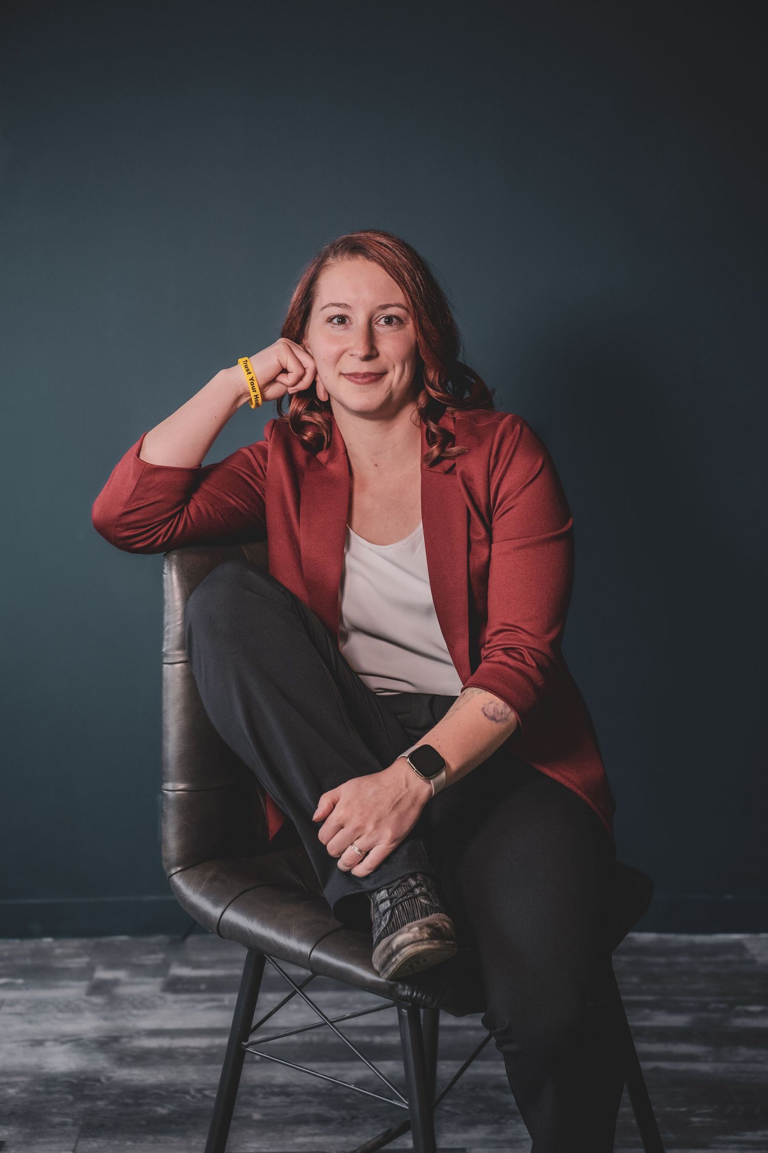 Woman in red blazer sitting cross-legged on chair smiling in studio setting during her commercial branding photoshoot.
