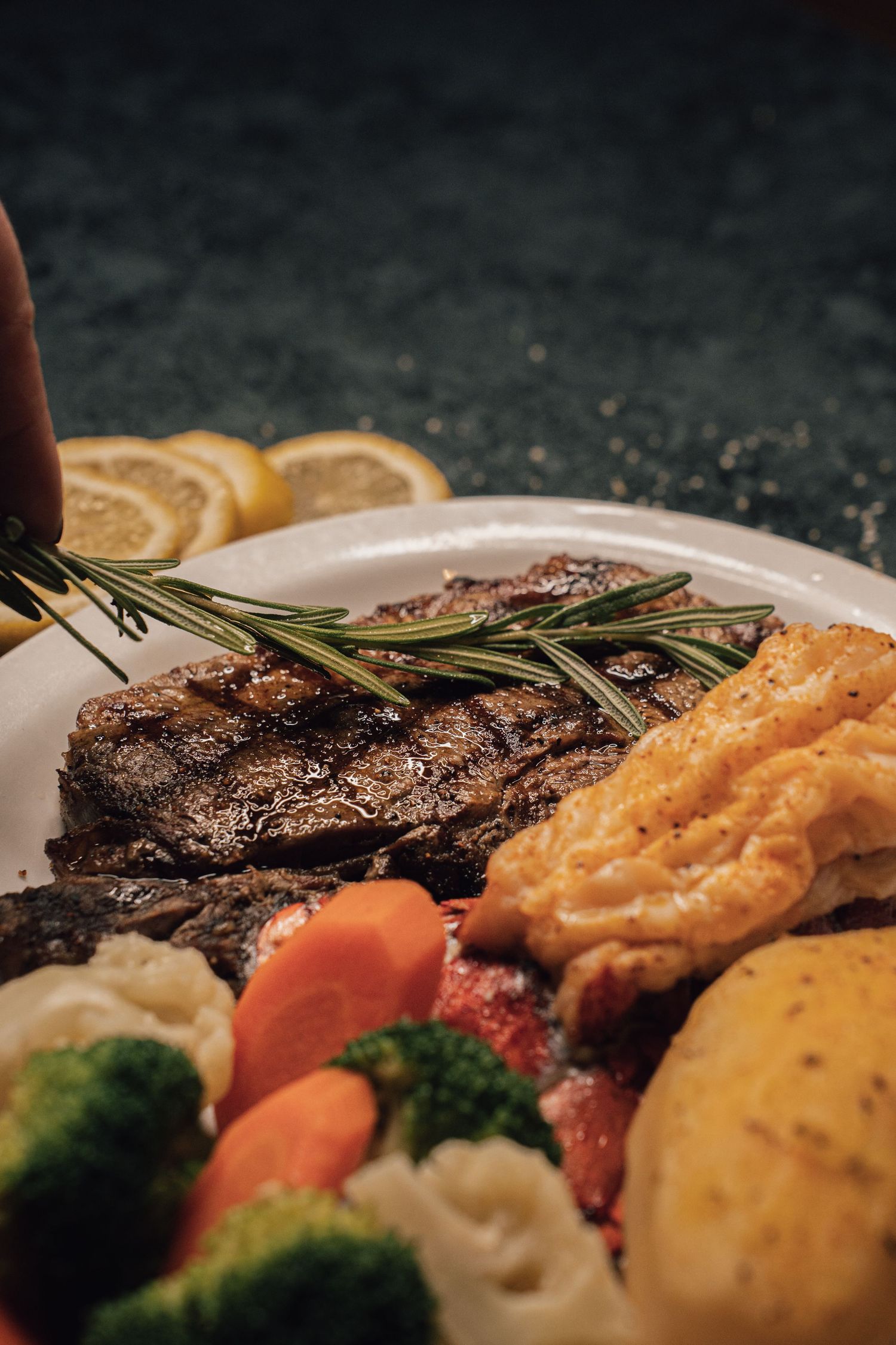Grilled steak garnished with rosemary and lemon, served with roasted vegetables and crispy potatoes.