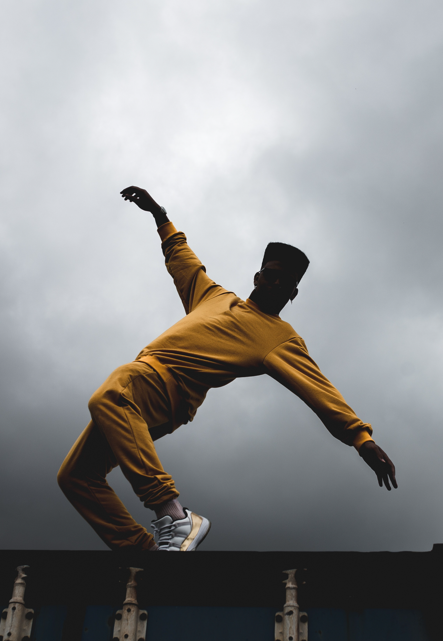Urban action portrait of a person mid-air, leaping dramatically from a ledge against a bright, overcast sky.