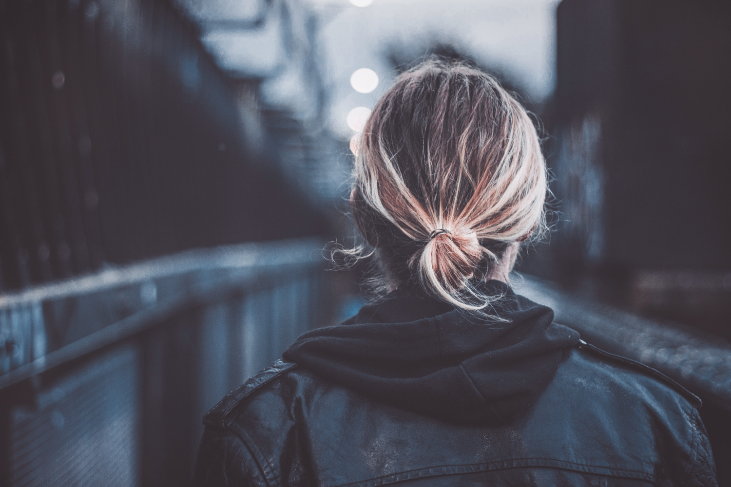 Moody, cinematic portrait shot from behind of an individual with a bun, wearing a dark hooded sweatshirt.