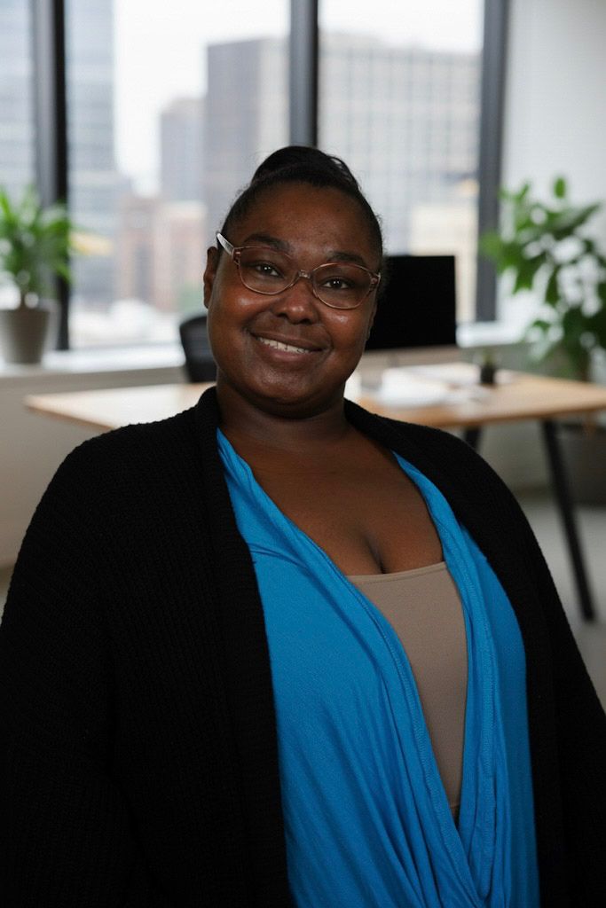 Professional business headshot of a smiling woman in a blue top, taken in a bright, modern office interior