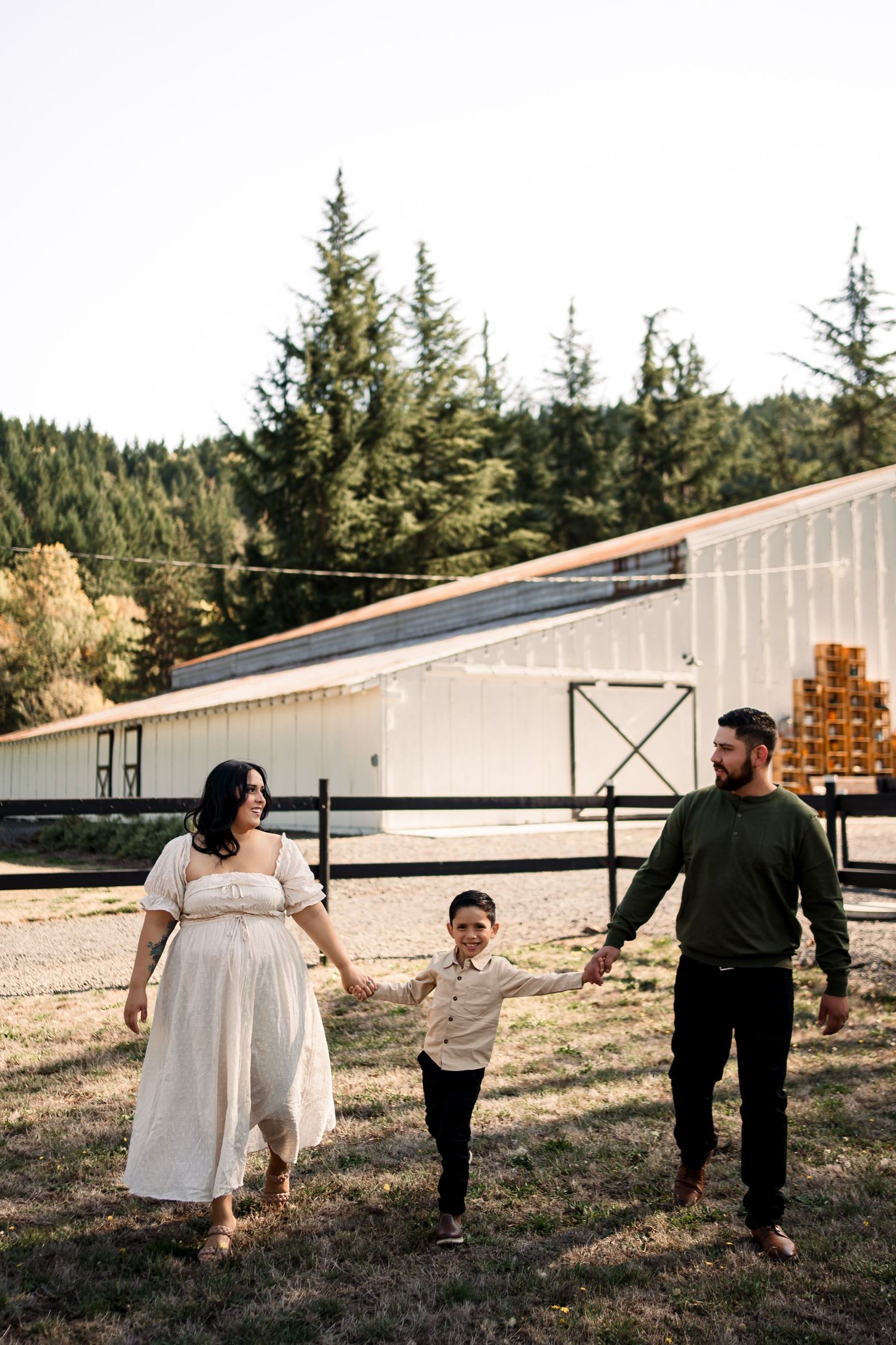 Family walking and playing together near white barn buildings.