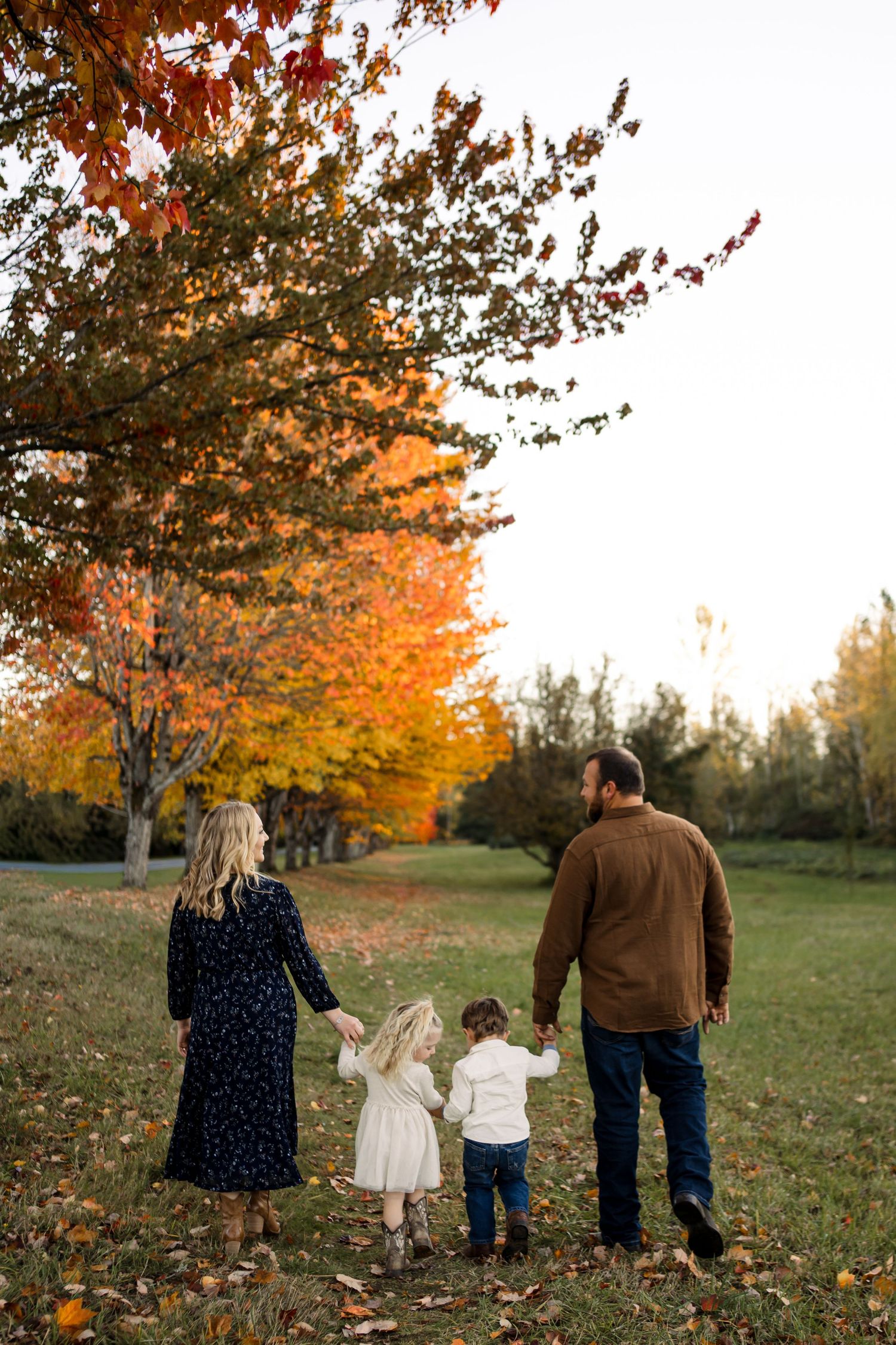 Family walking together through autumn trees with vibrant orange foliage.