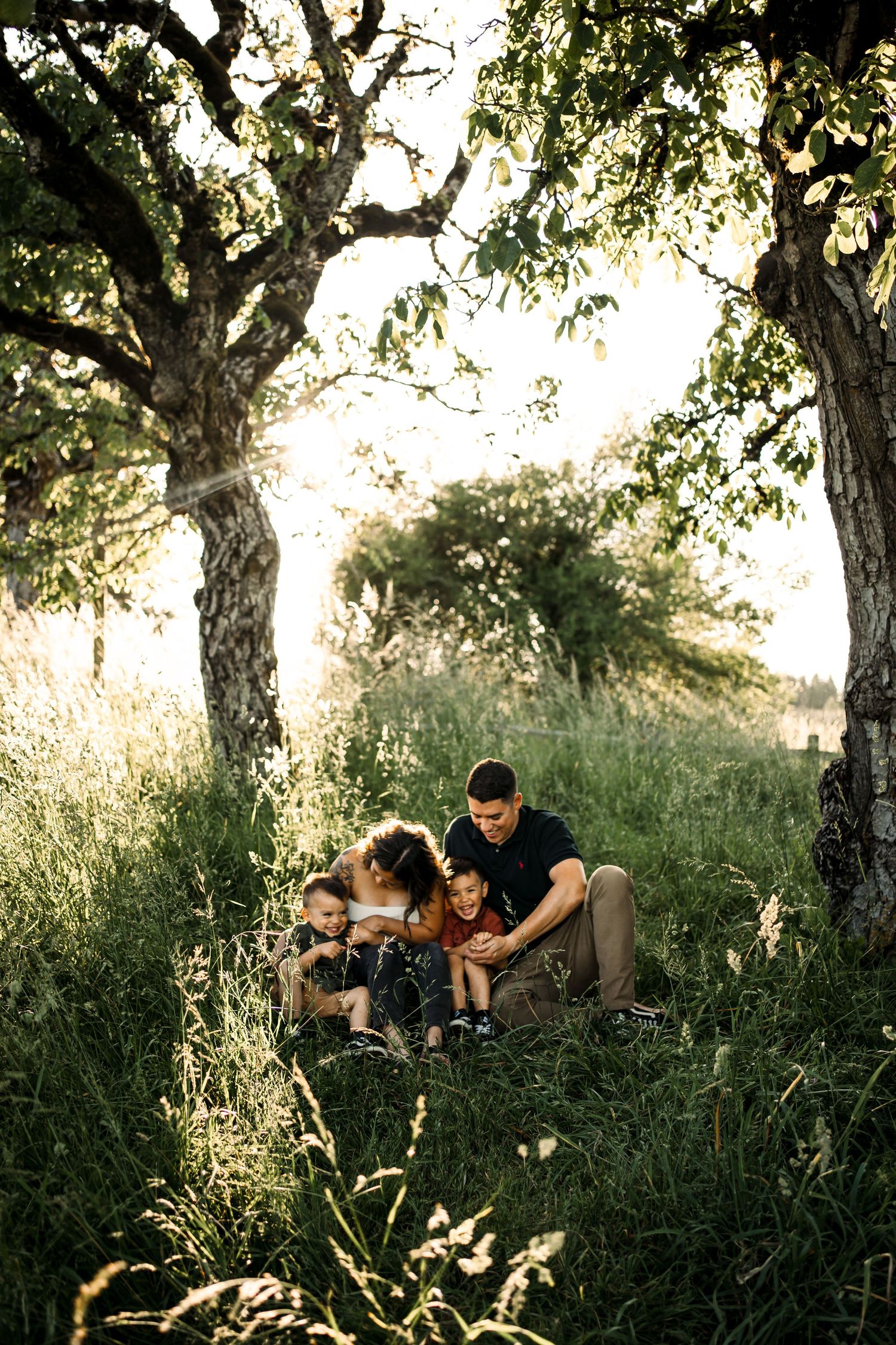 Family relaxing under trees during outdoor photo session.