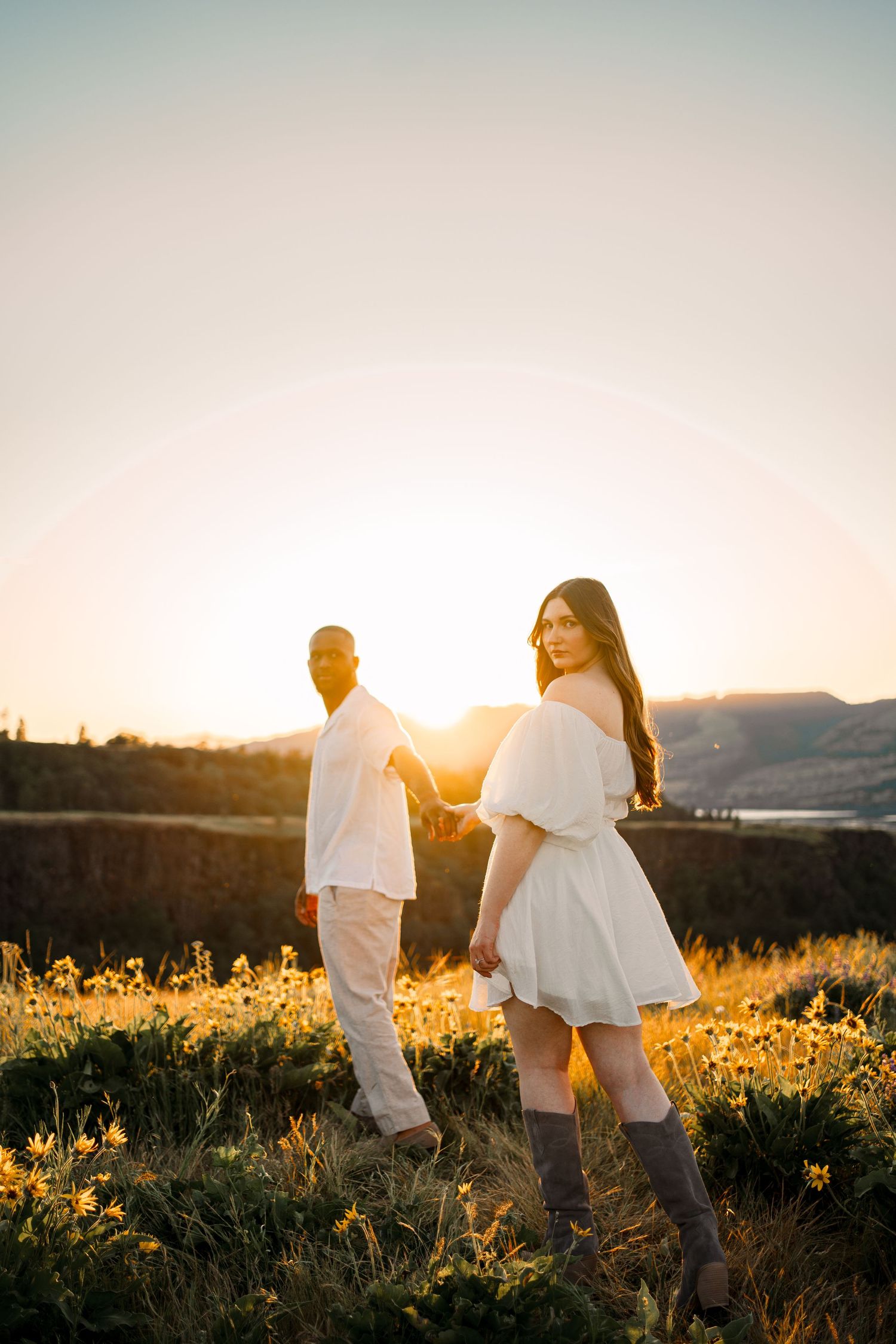 Couple strolls through a sunlit meadow wearing coordinated white outfits.