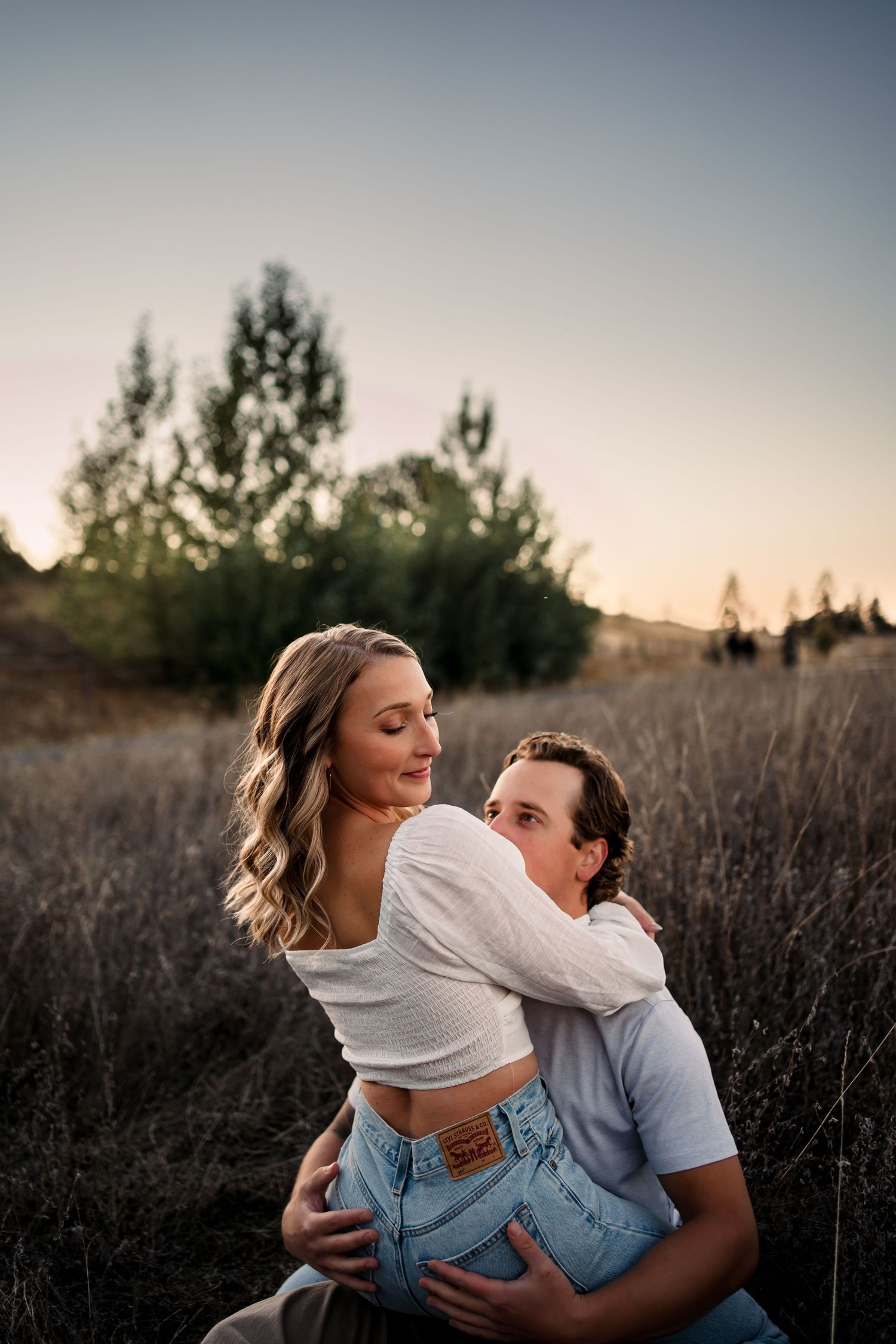 Romantic couple embraces in a field of tall grass during golden hour sunset.