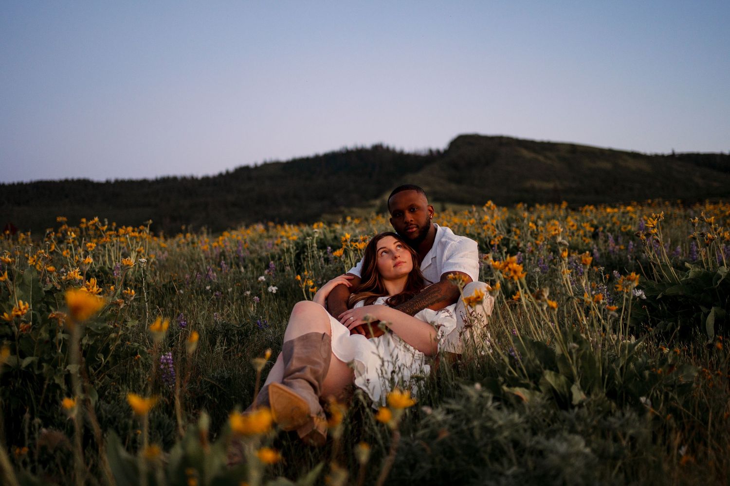 Romantic couple poses in a field of yellow wildflowers during sunset.