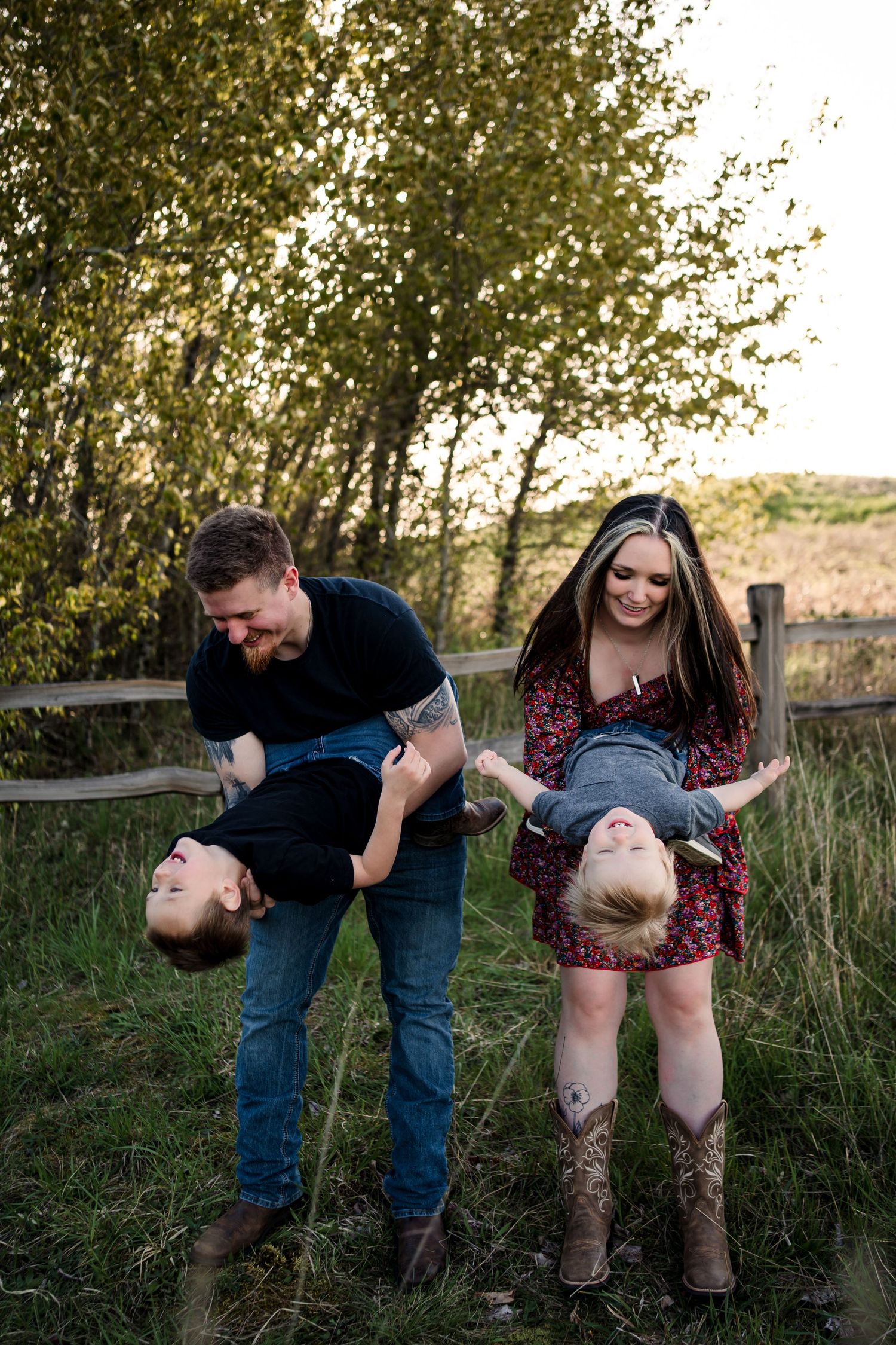 Family playing and laughing together near a wooden fence at sunset.