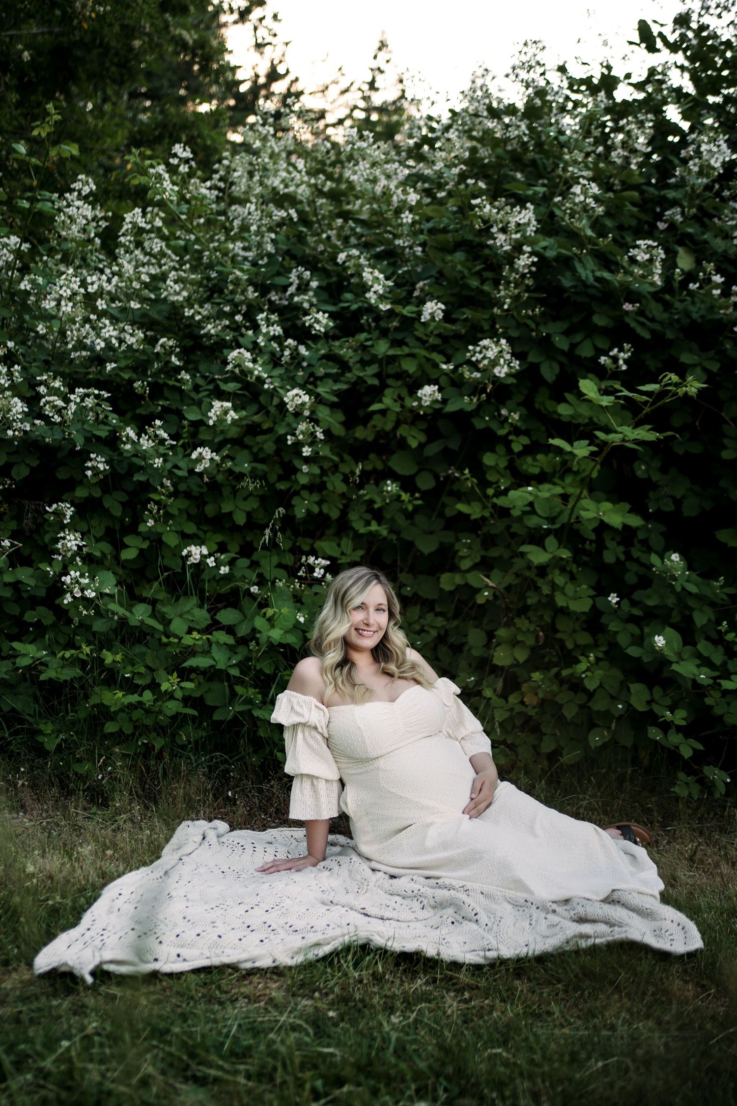 A person in white lace reclines gracefully on grass amid blooming flowers.
