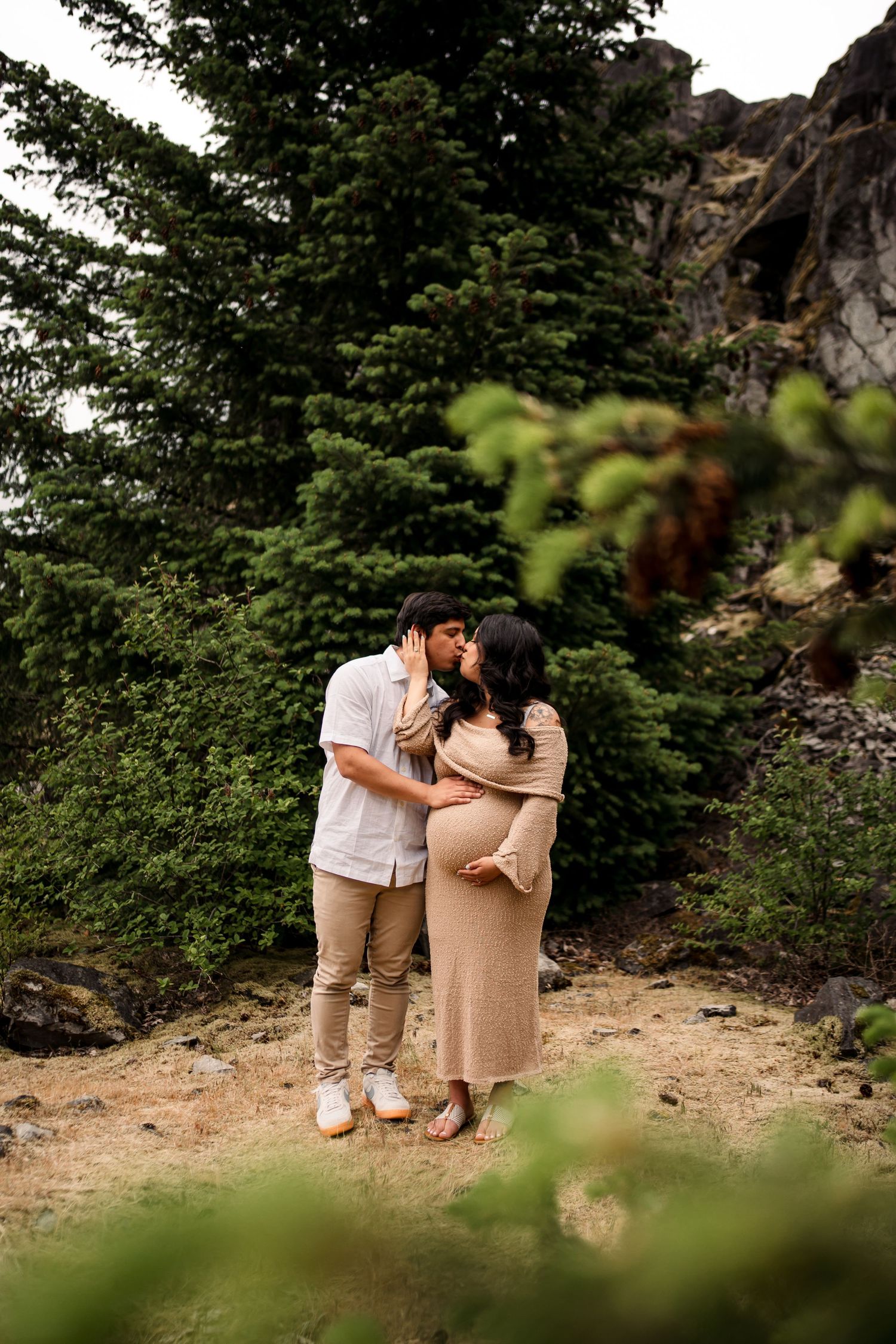 A couple shares an intimate moment on a mountain trail surrounded by evergreen trees.