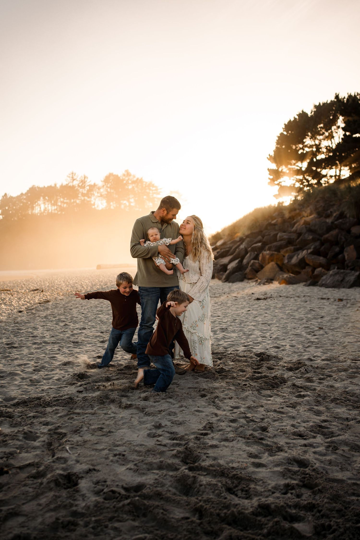 A family shares an intimate moment together on a beach at sunset with rocky cliffs in the background.