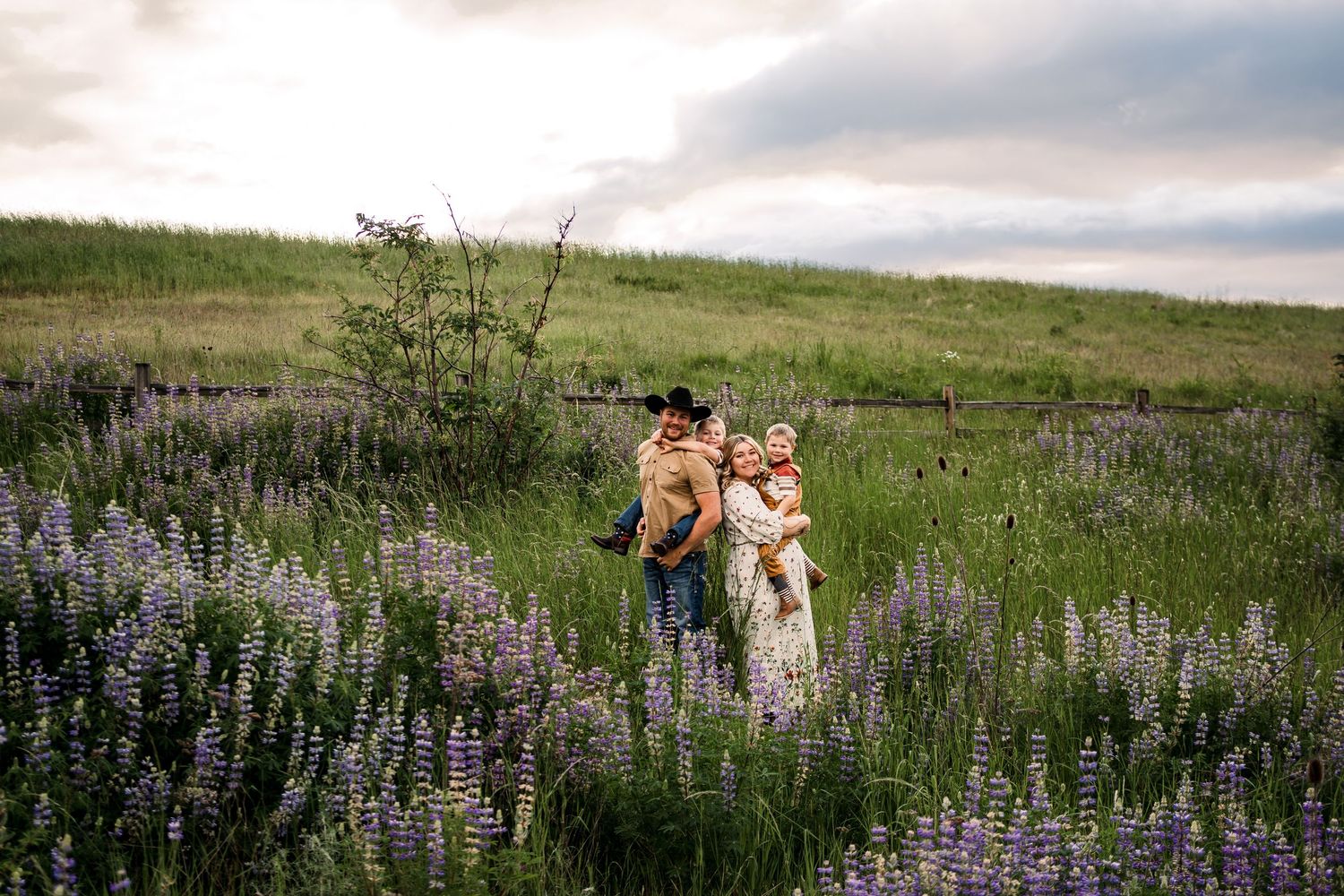 A couple stands together in a meadow of purple lupines during golden hour.