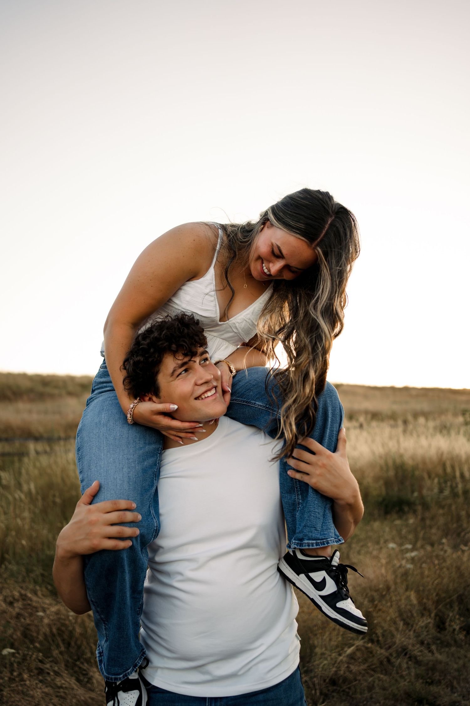 Intimate couple shares playful moments in casual denim and white outfits outdoors.