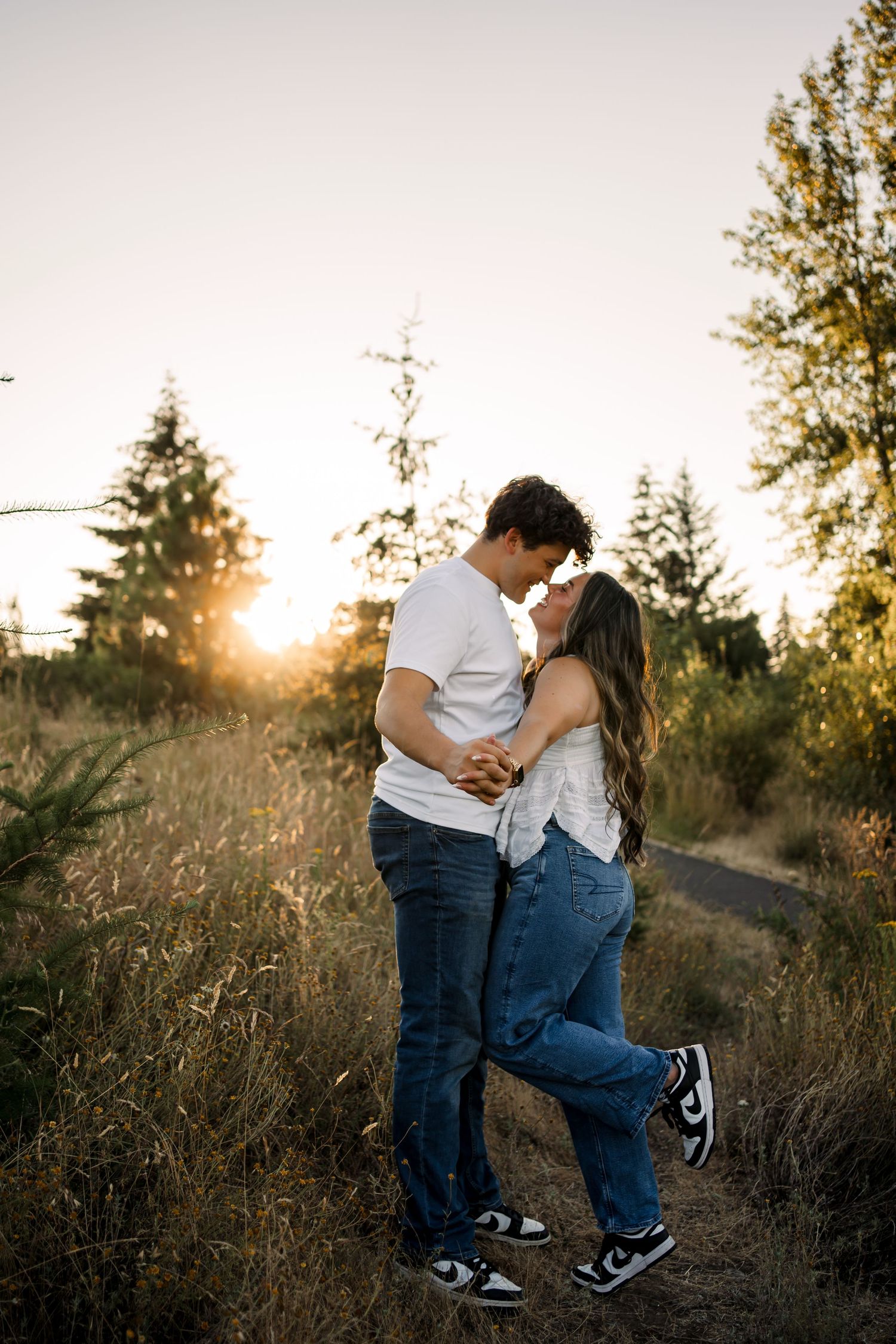 Playful couple in casual wear shares intimate moments on a sunset trail.