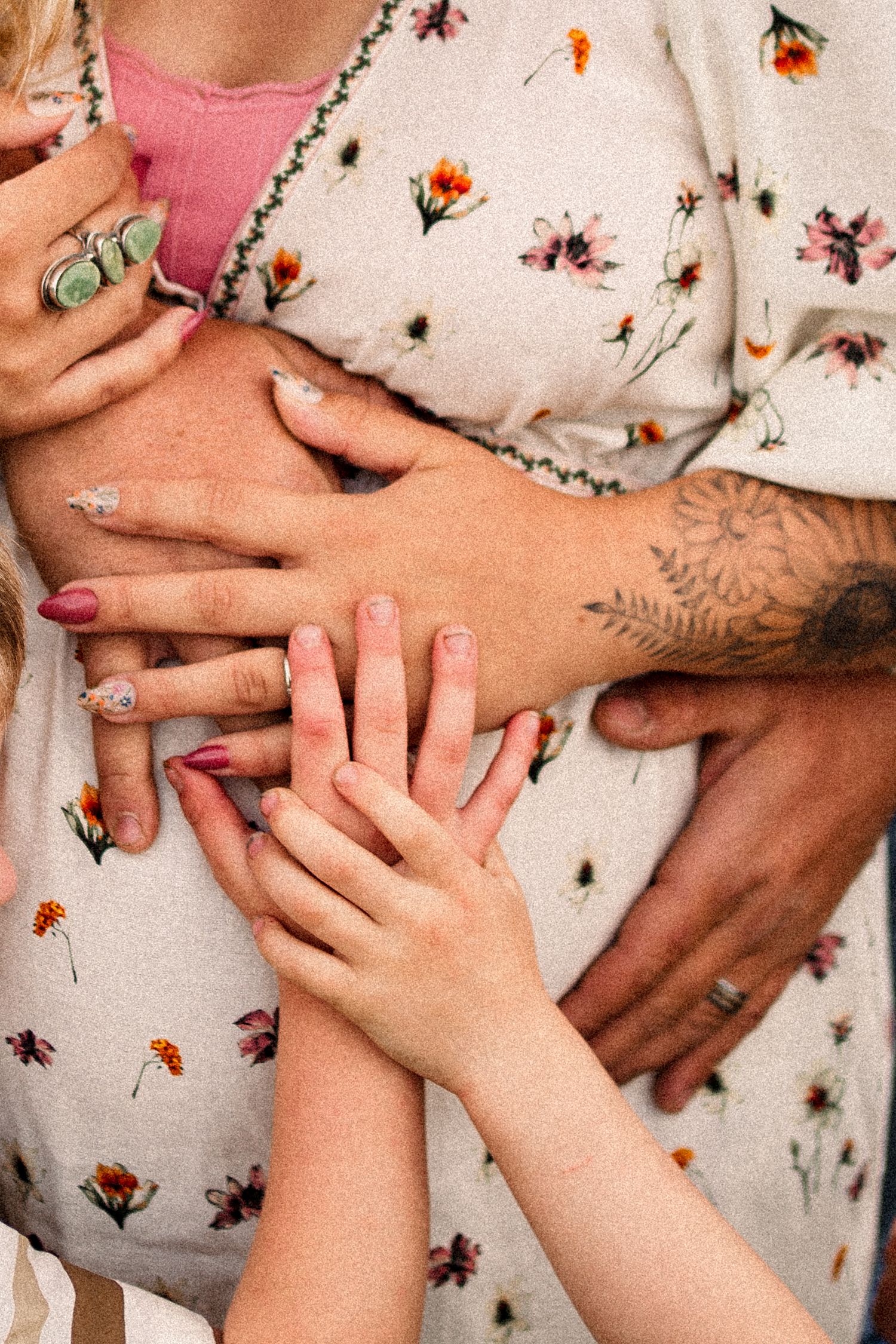 Multiple hands rest lovingly on a floral dress fabric in a tender moment.