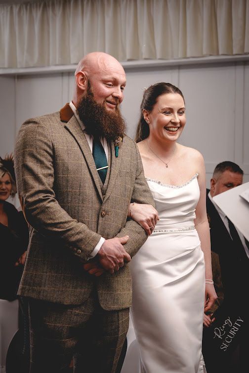 A couple shares a joyful moment during their wedding celebration, with the groom wearing a brown tweed suit.