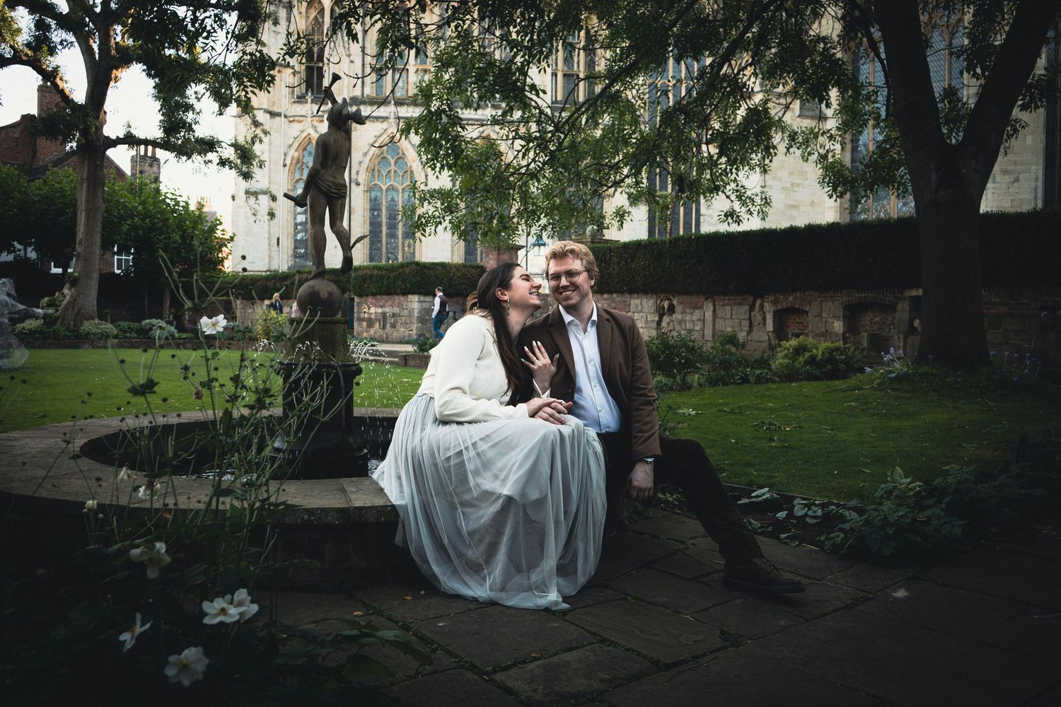 A couple in formal wedding attire poses together in a scenic garden setting during their outdoor photoshoot.