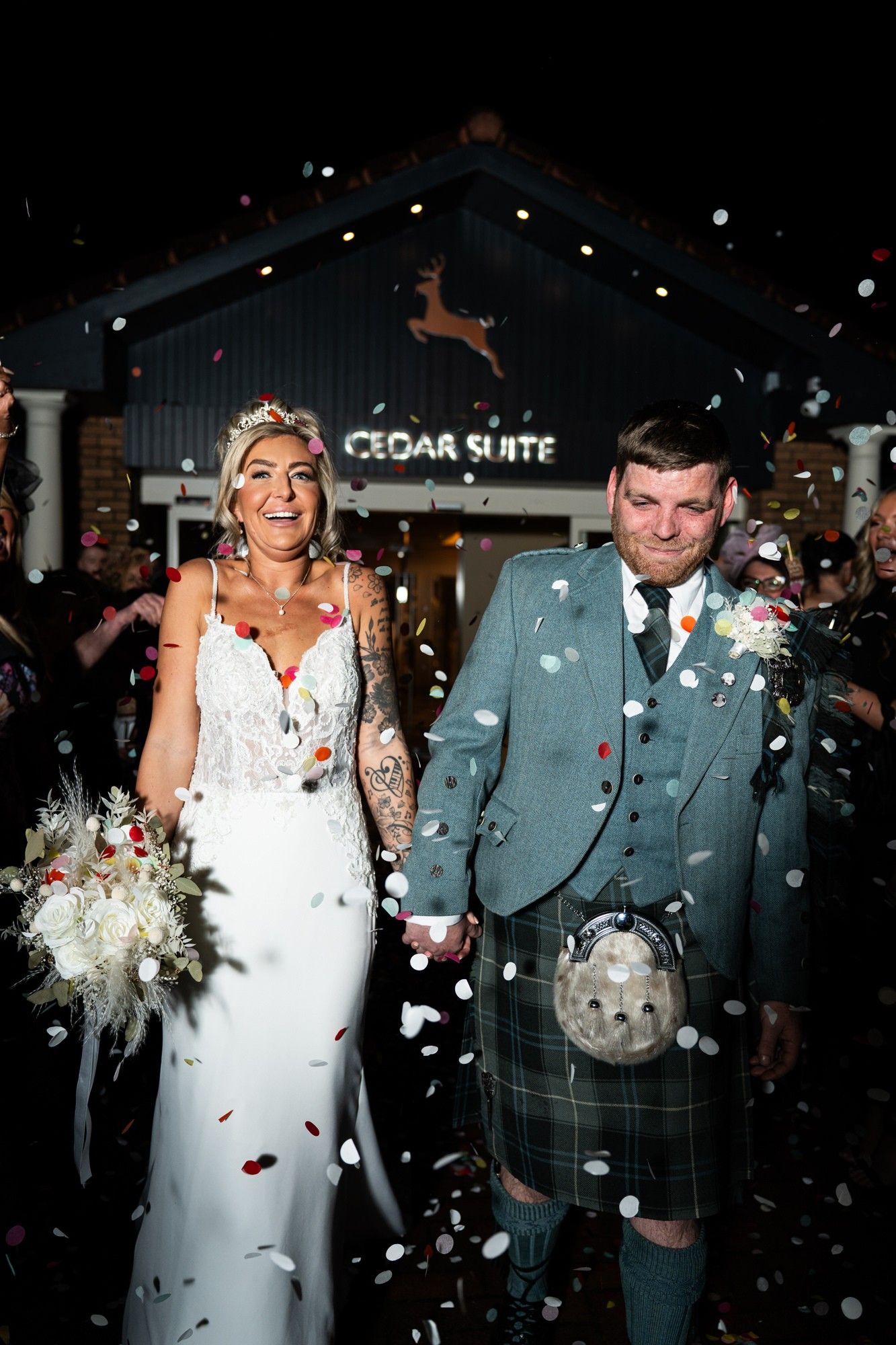 A wedding couple exits their ceremony at Cedar Suite while guests shower them with confetti in a nighttime celebration.