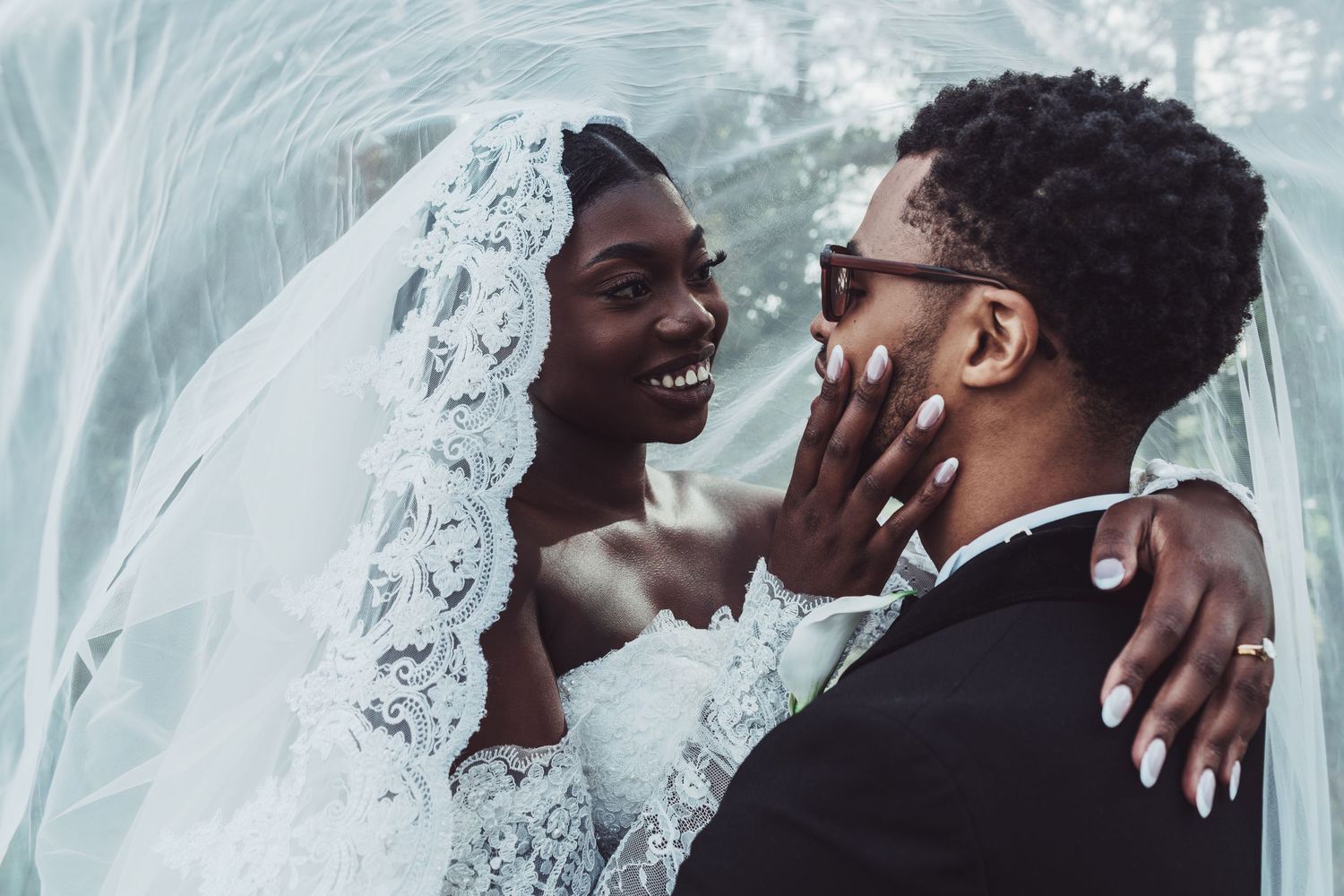A joyful Black bride and groom share an intimate moment under a flowing white veil on their wedding day.