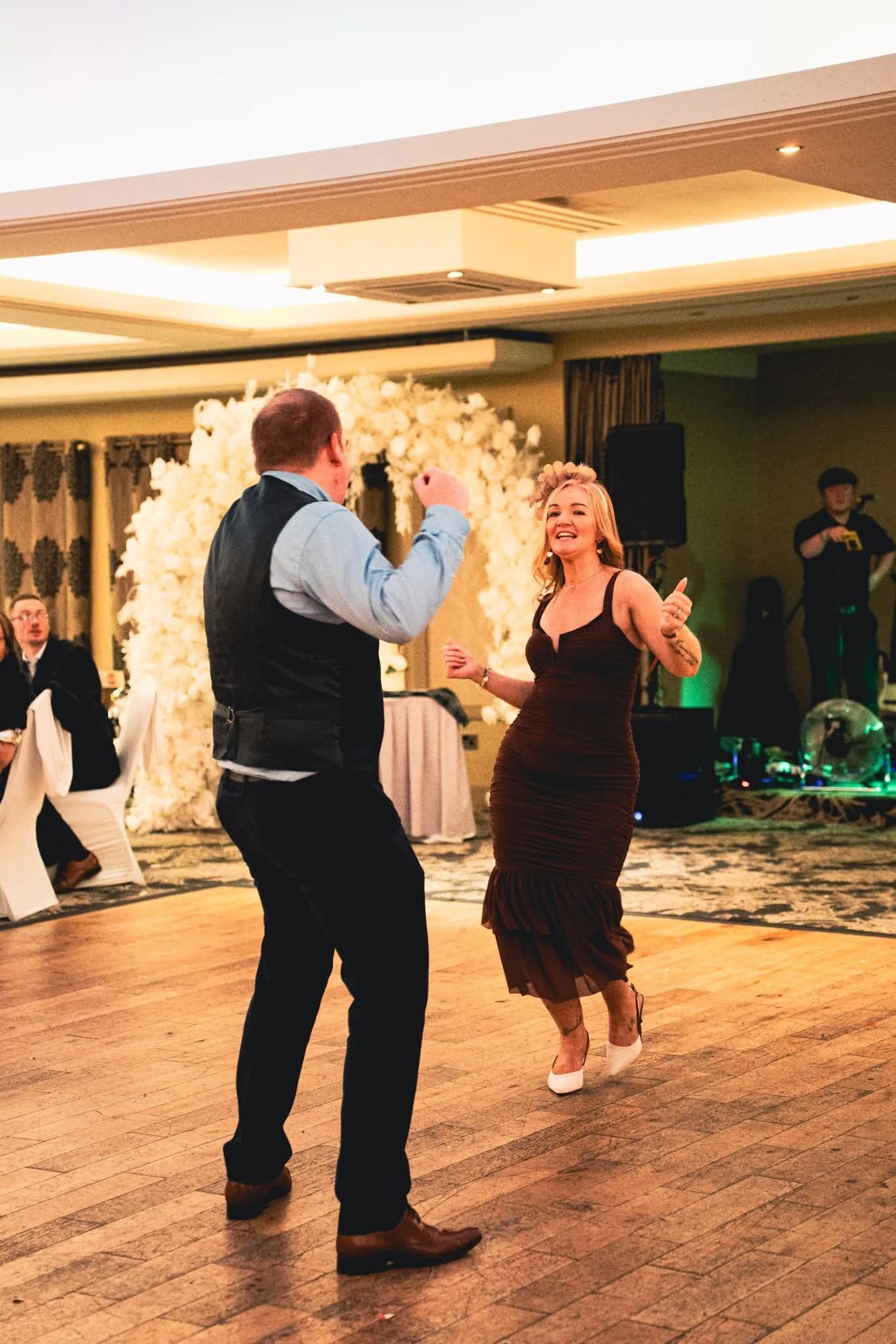 Couples dancing together on a wooden dance floor at an elegant indoor event venue with warm lighting.