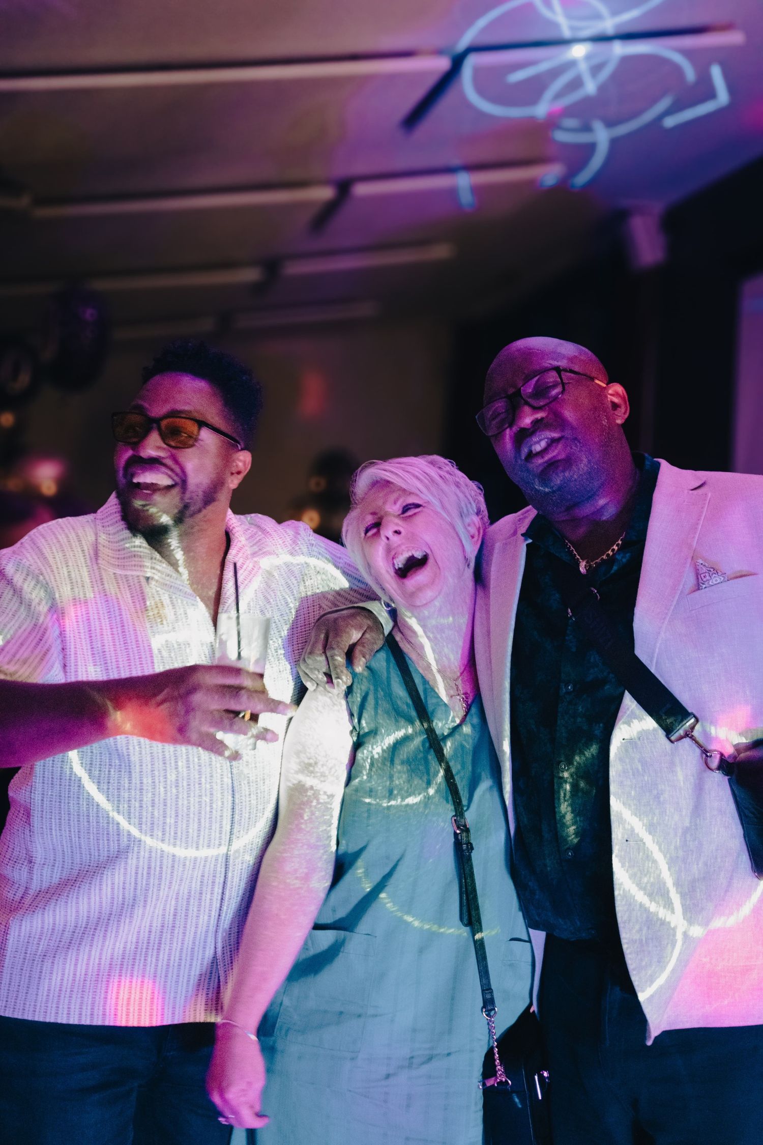 Performers in white shirts and dark vests sing together on stage under purple lighting at a concert venue.