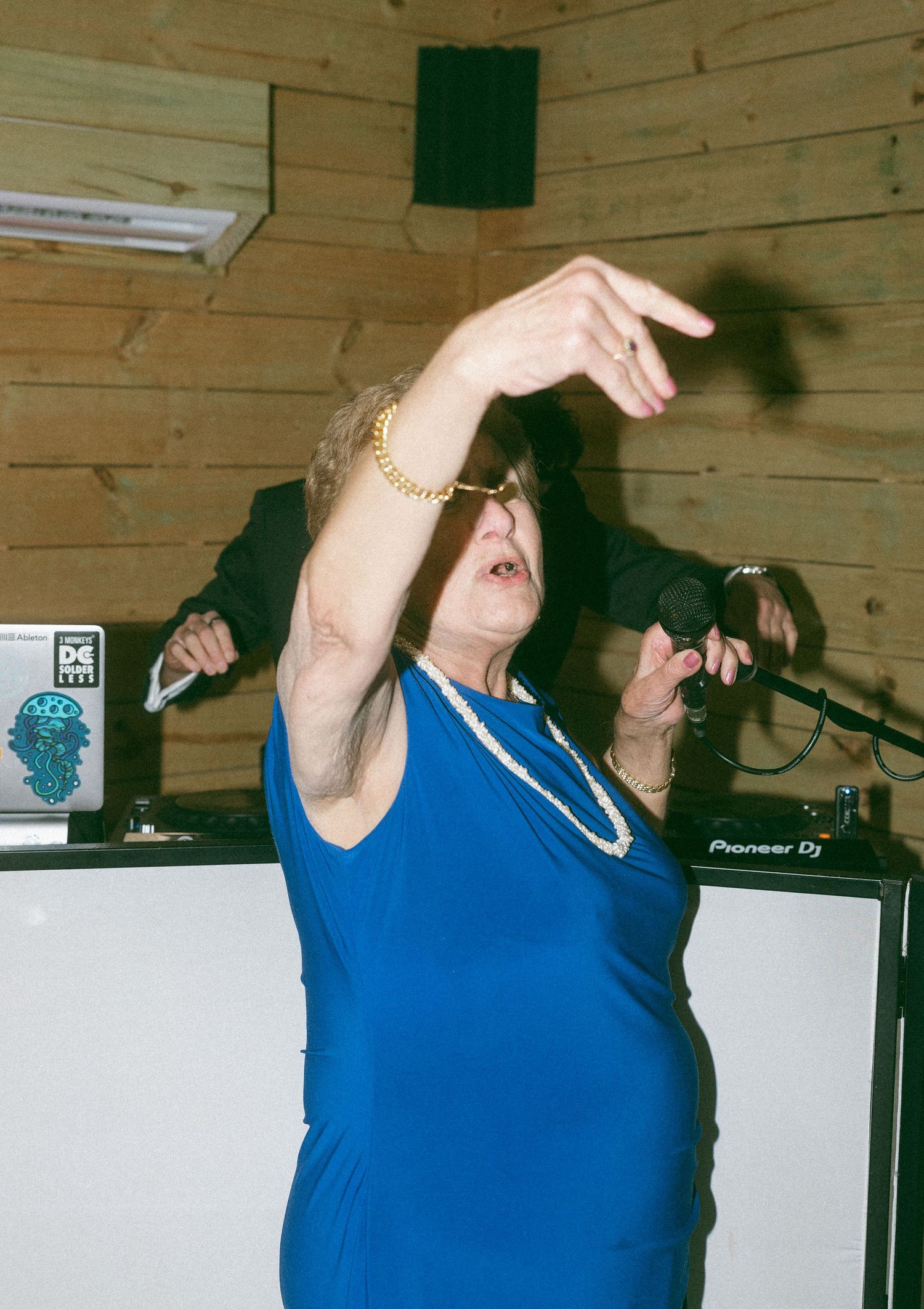 Older woman in blue dress dancing enthusiastically near DJ equipment at a wedding reception.