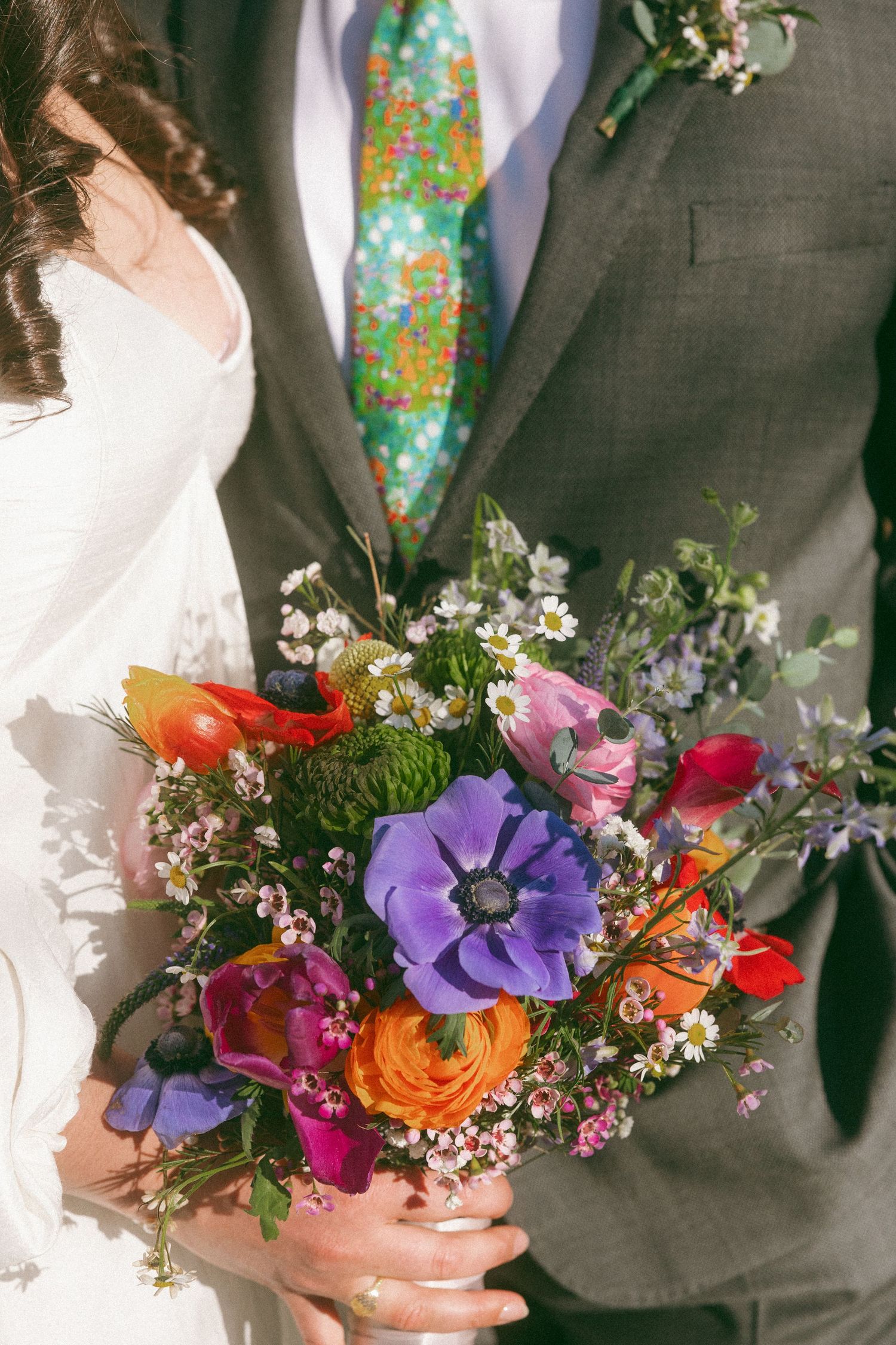 Bride and groom holding a vibrant wildflower wedding bouquet with purple anemones, red tulips, and orange ranunculus.