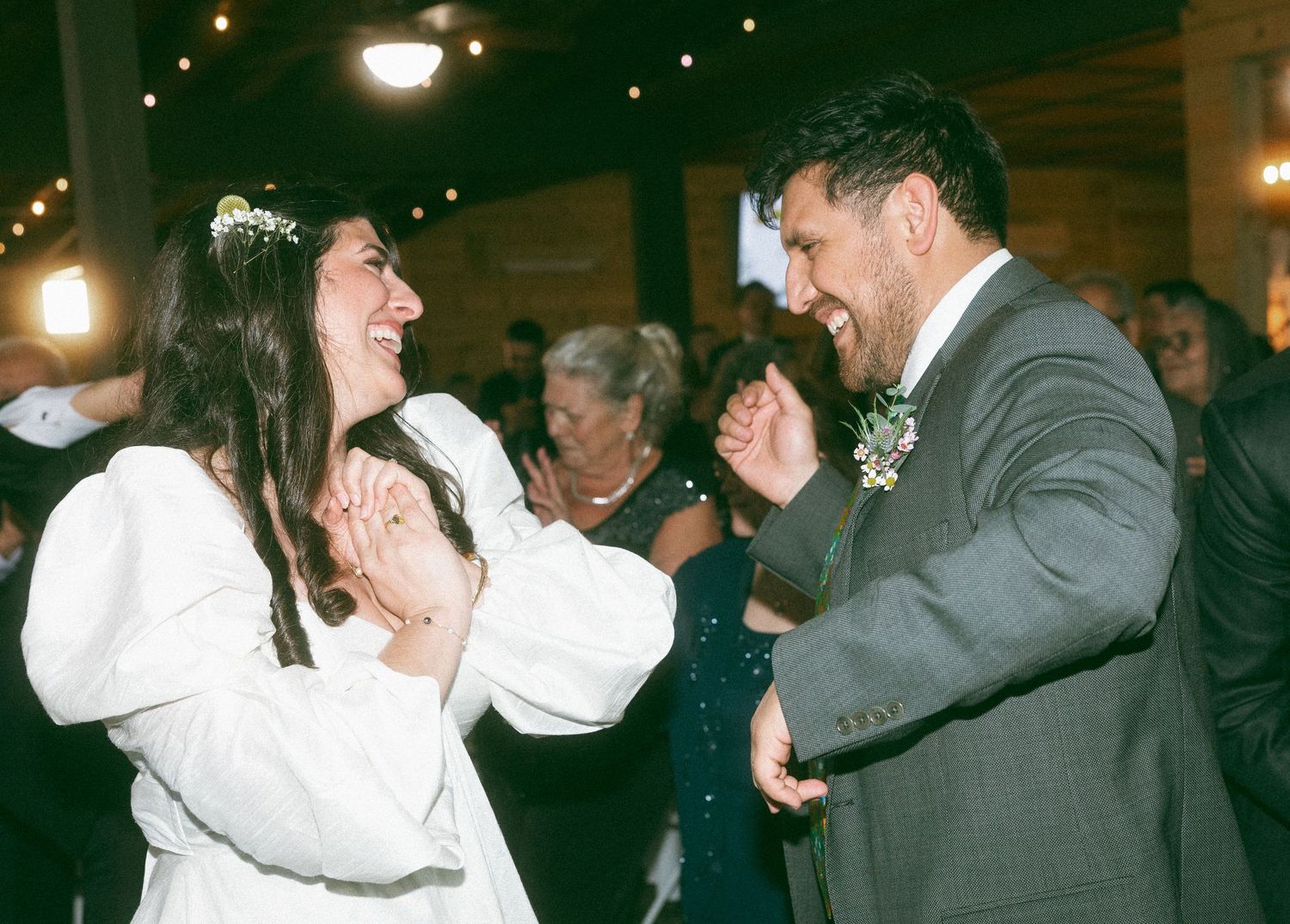 Bride and groom laughing joyfully during first dance at wedding reception in rustic venue.