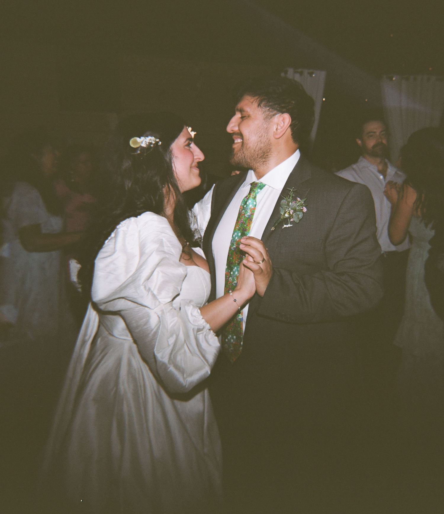 Bride and groom share their first dance at wedding reception, bride in white gown with floral crown, groom in gray suit.