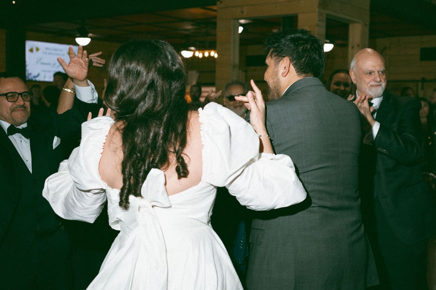 Bride in white gown dancing with groom in suit at elegant wedding reception with guests in formal attire.