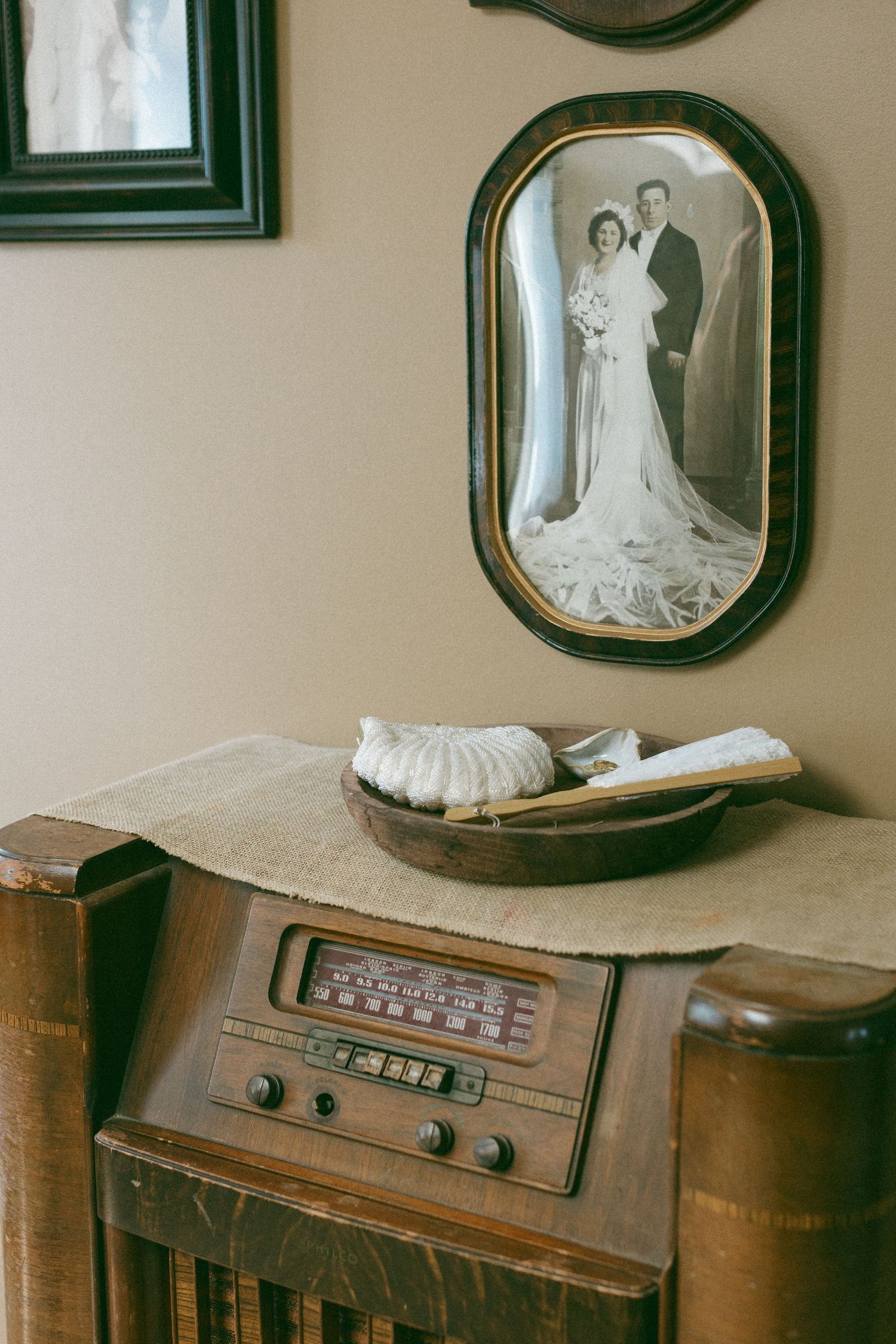Vintage radio cabinet with antique black and white wedding portrait in ornate oval frame on wall.