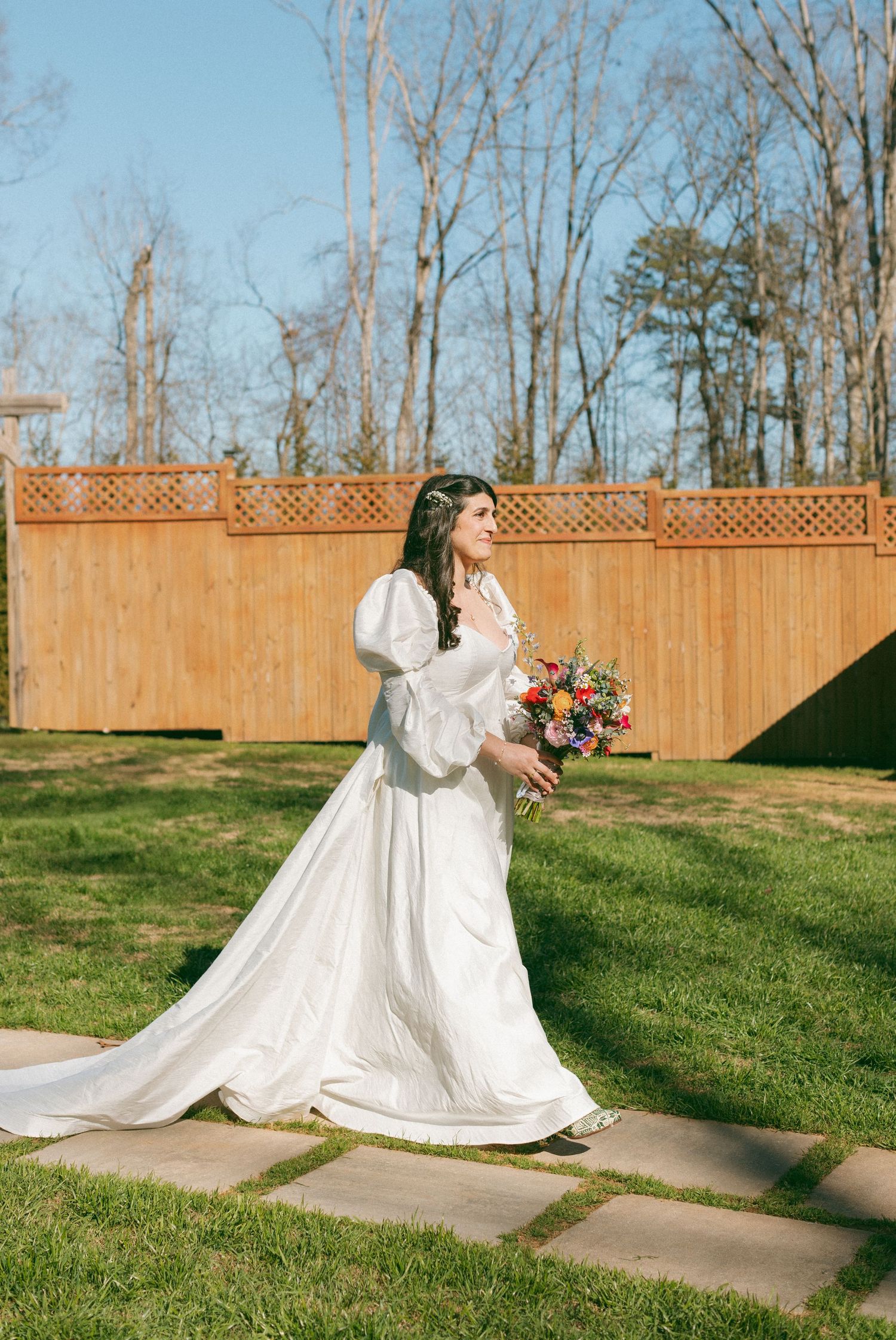 Elegant bride in a white puff-sleeve gown holding a colorful bouquet at an outdoor wedding.