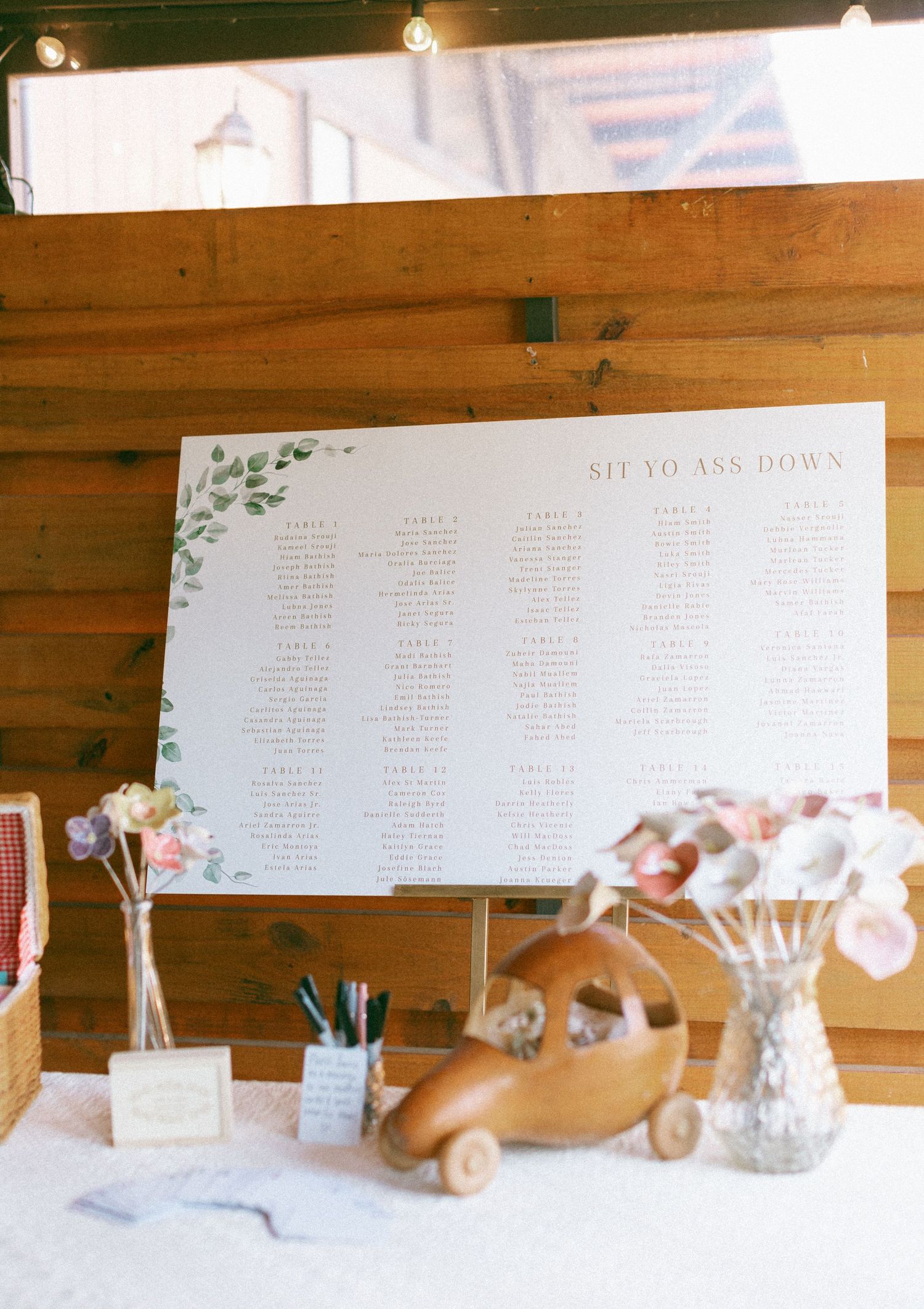 Elegant wedding seating chart display with floral accents and decorative items on a rustic wooden table.