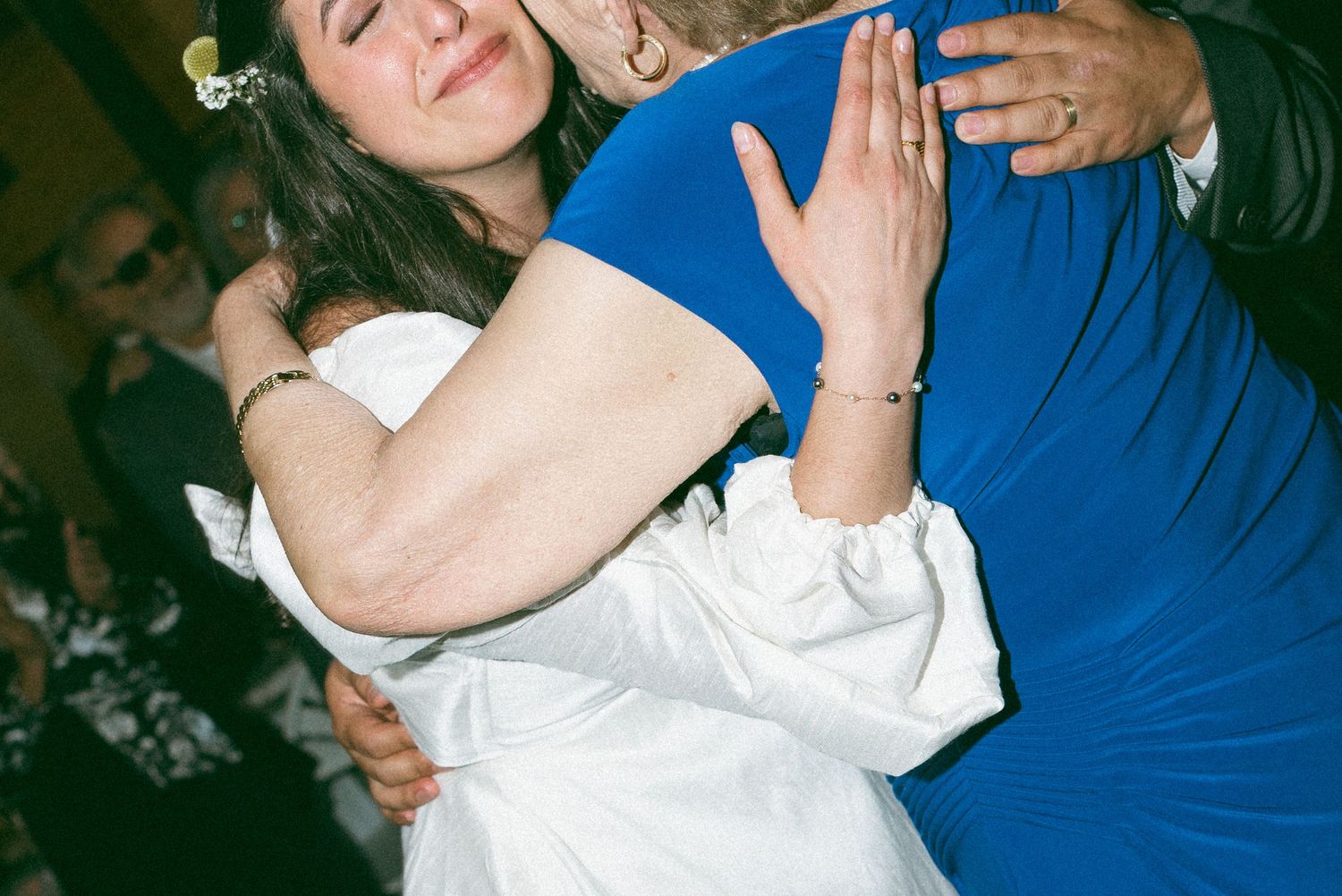 Bride in white dress sharing an emotional hug with guest in blue outfit during wedding reception dance.