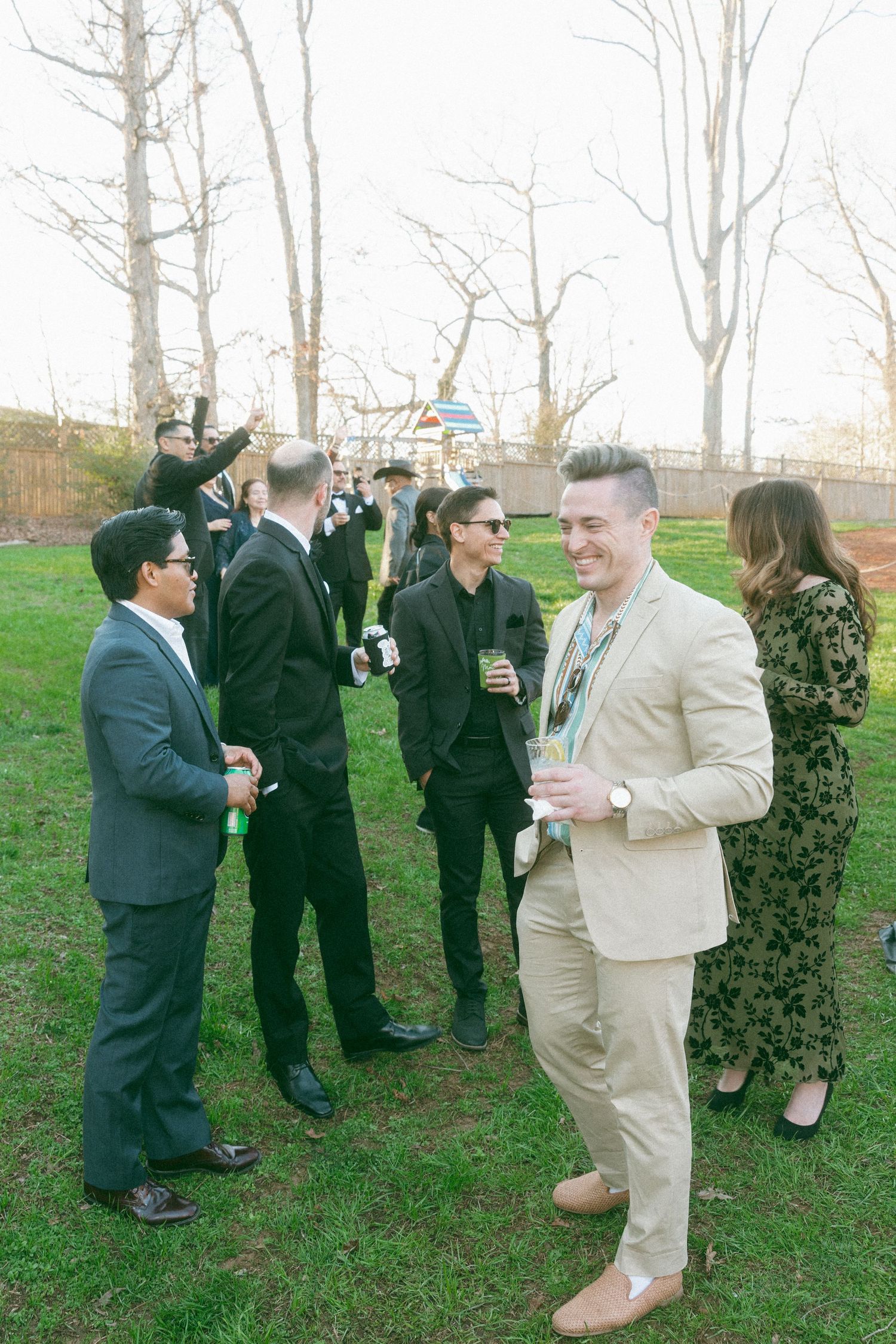 Wedding guests socializing outdoors on a sunny day, dressed in formal attire on green grass.