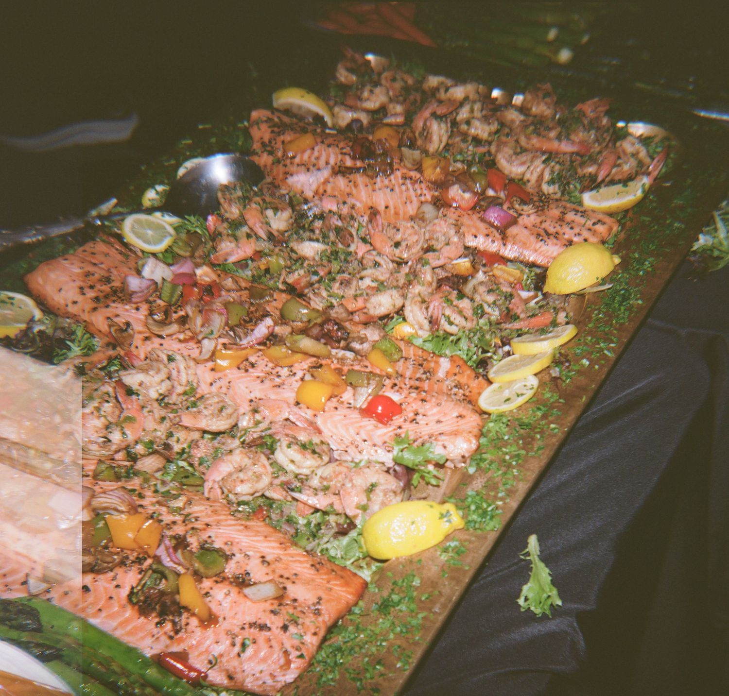 Grilled salmon fillets topped with herbs, lemon slices, and colorful vegetables on a large wooden serving board.