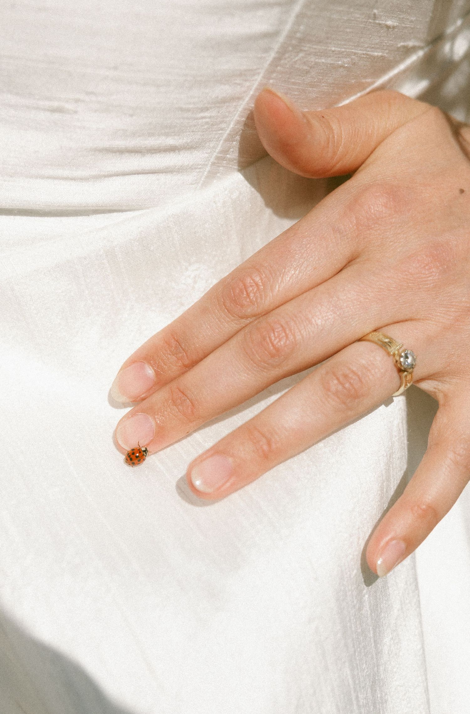 Close-up of bride's hand resting on white wedding dress with diamond and gold engagement ring.