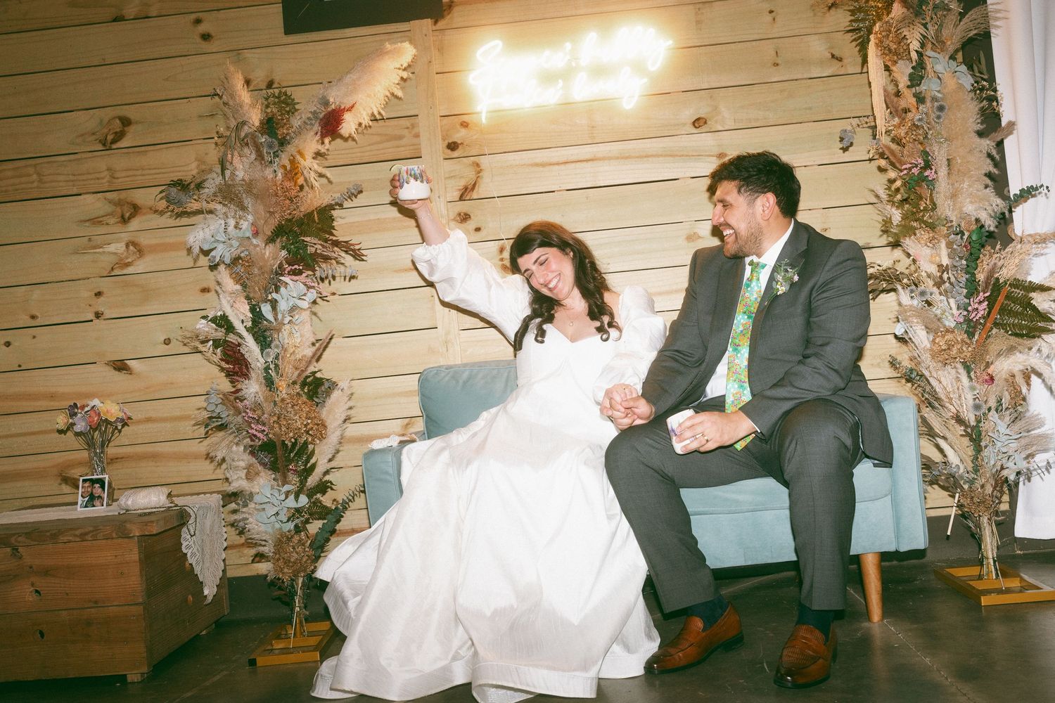 Bride and groom sitting on a blue sofa celebrating at their rustic barn wedding reception.