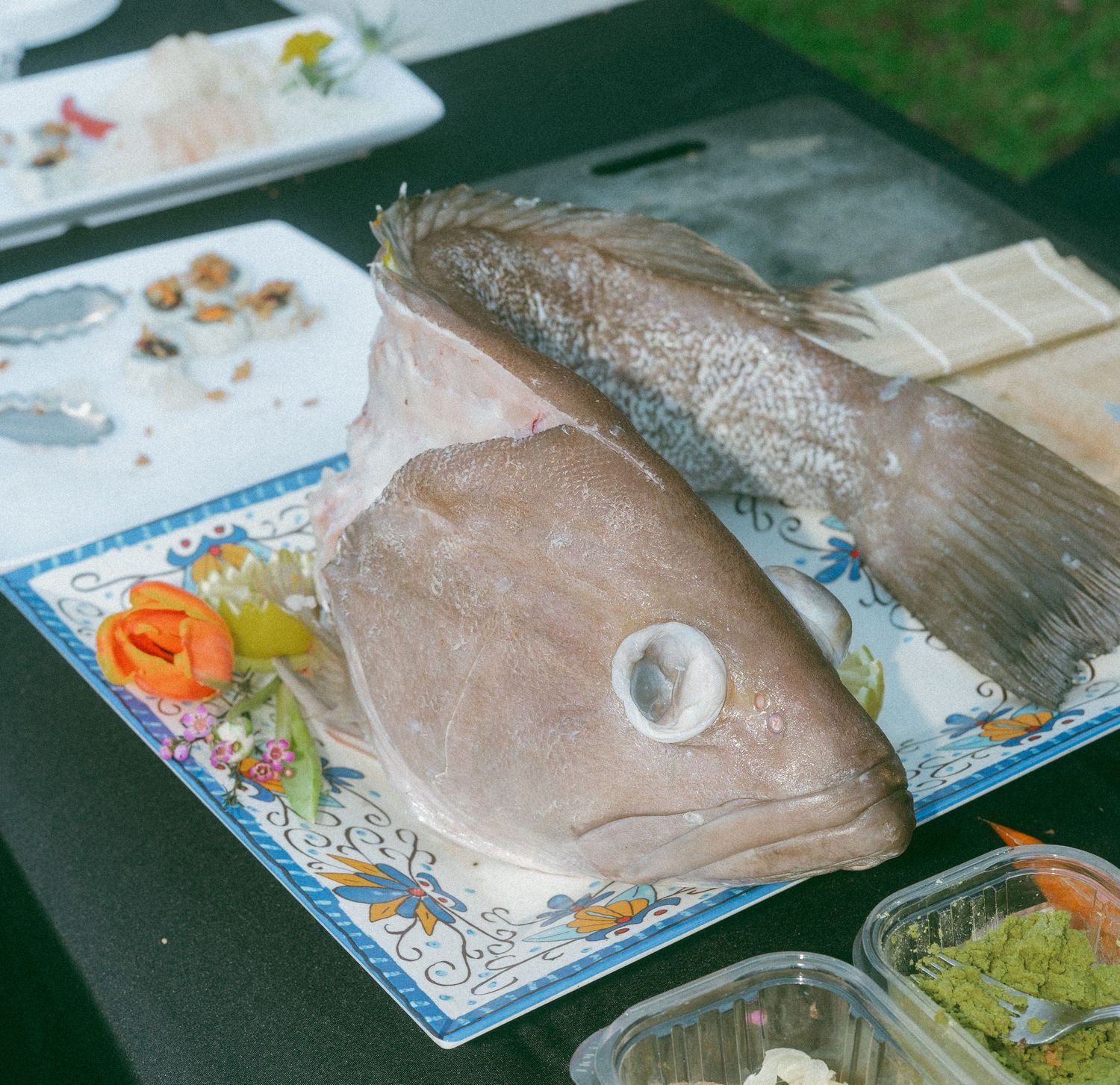 Fresh whole fish head displayed on a decorative plate at an outdoor food event with garnishes.