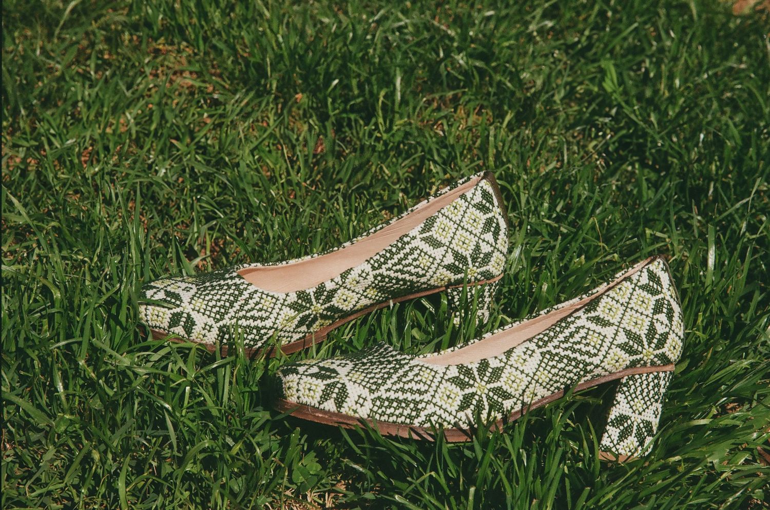 Green and white patterned block heel pumps resting on lush green grass outdoors.