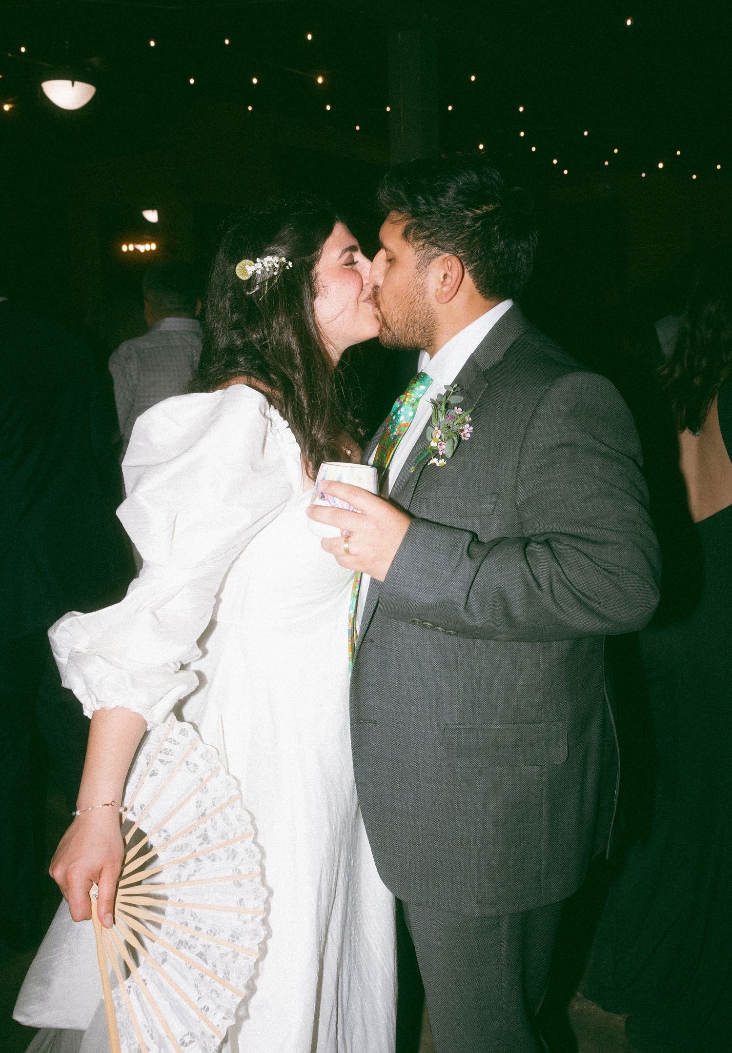 Bride and groom sharing a romantic kiss at their wedding reception, bride holding a decorative fan.