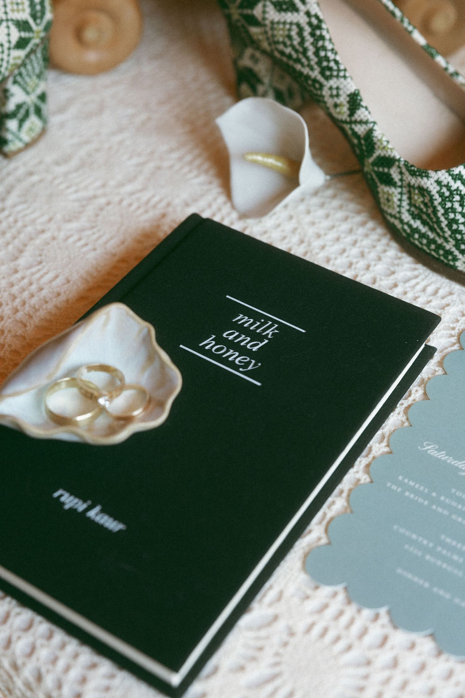 Milk and Honey poetry book by Rupi Kaur on a white knit blanket with gold wedding rings and green patterned ribbon.