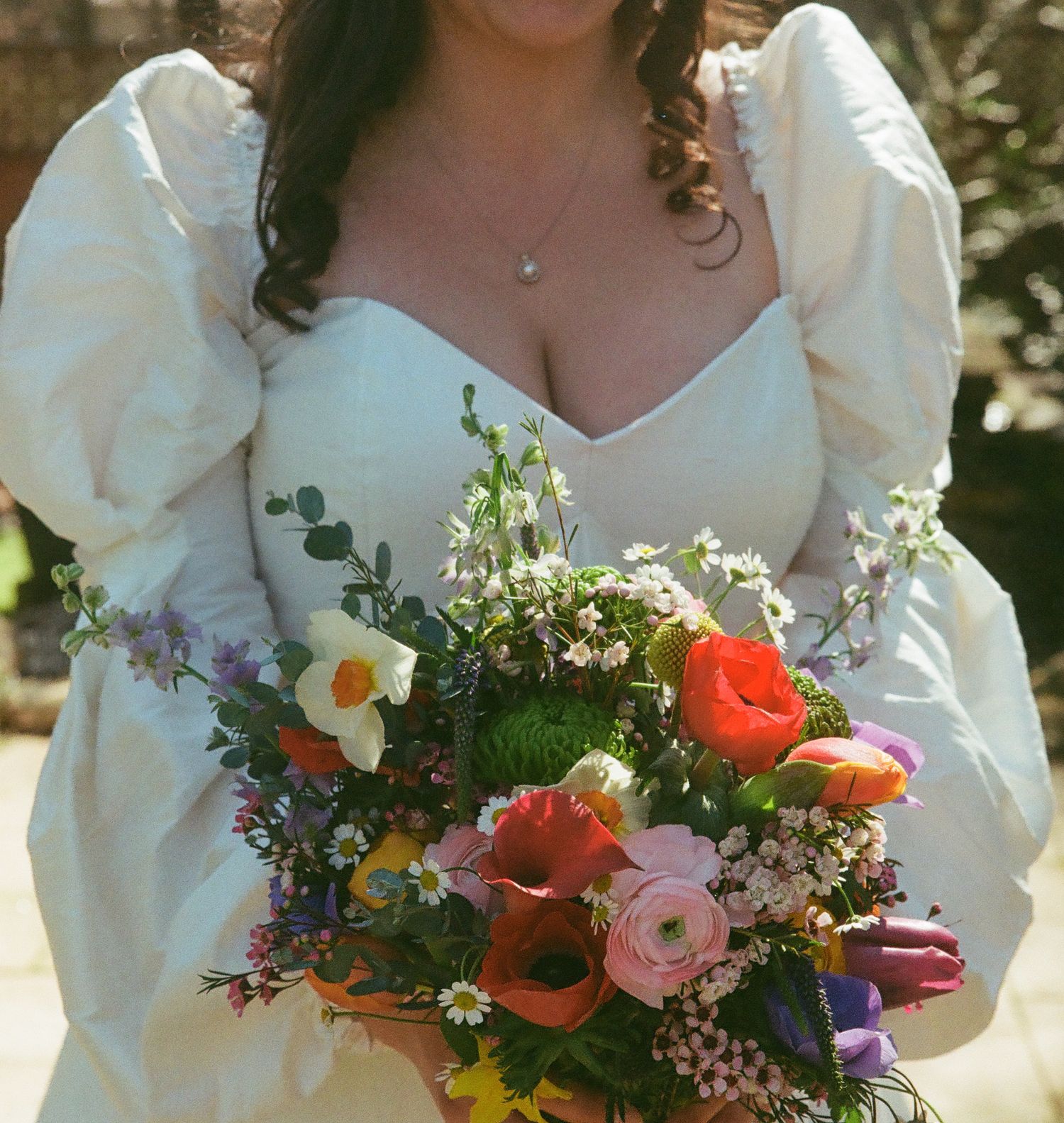 Bride in white dress with puffed sleeves holding a colorful wildflower bouquet with orange, pink, and purple blooms.