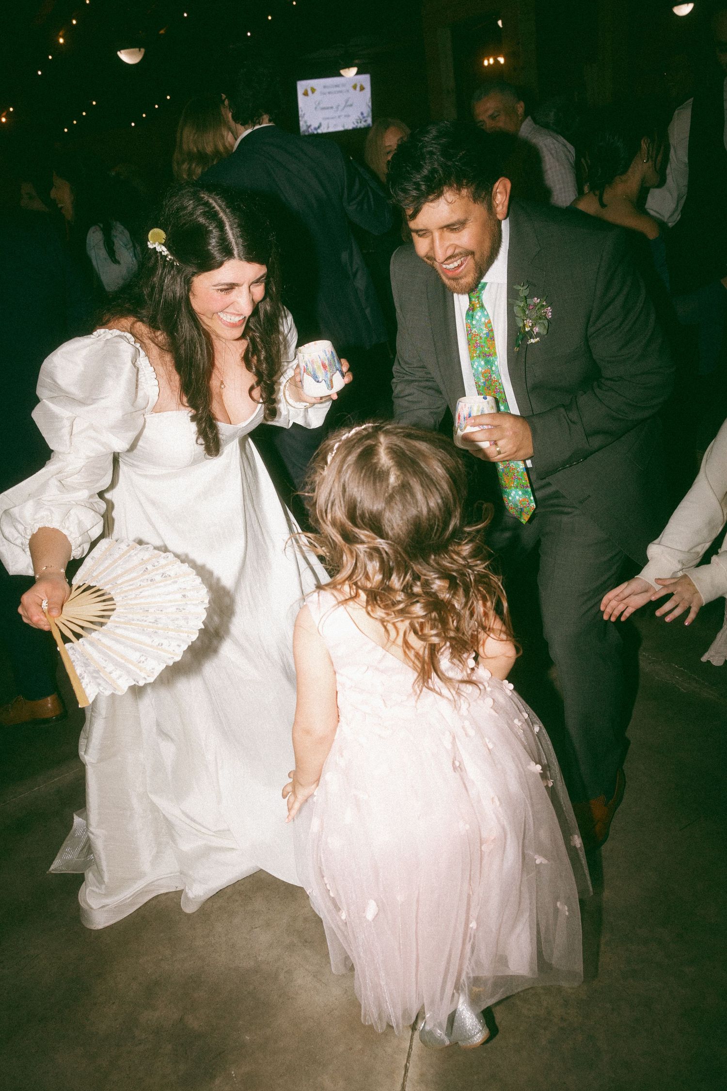 Bride and groom dancing with a young flower girl in a pink tutu dress at a lively wedding reception.